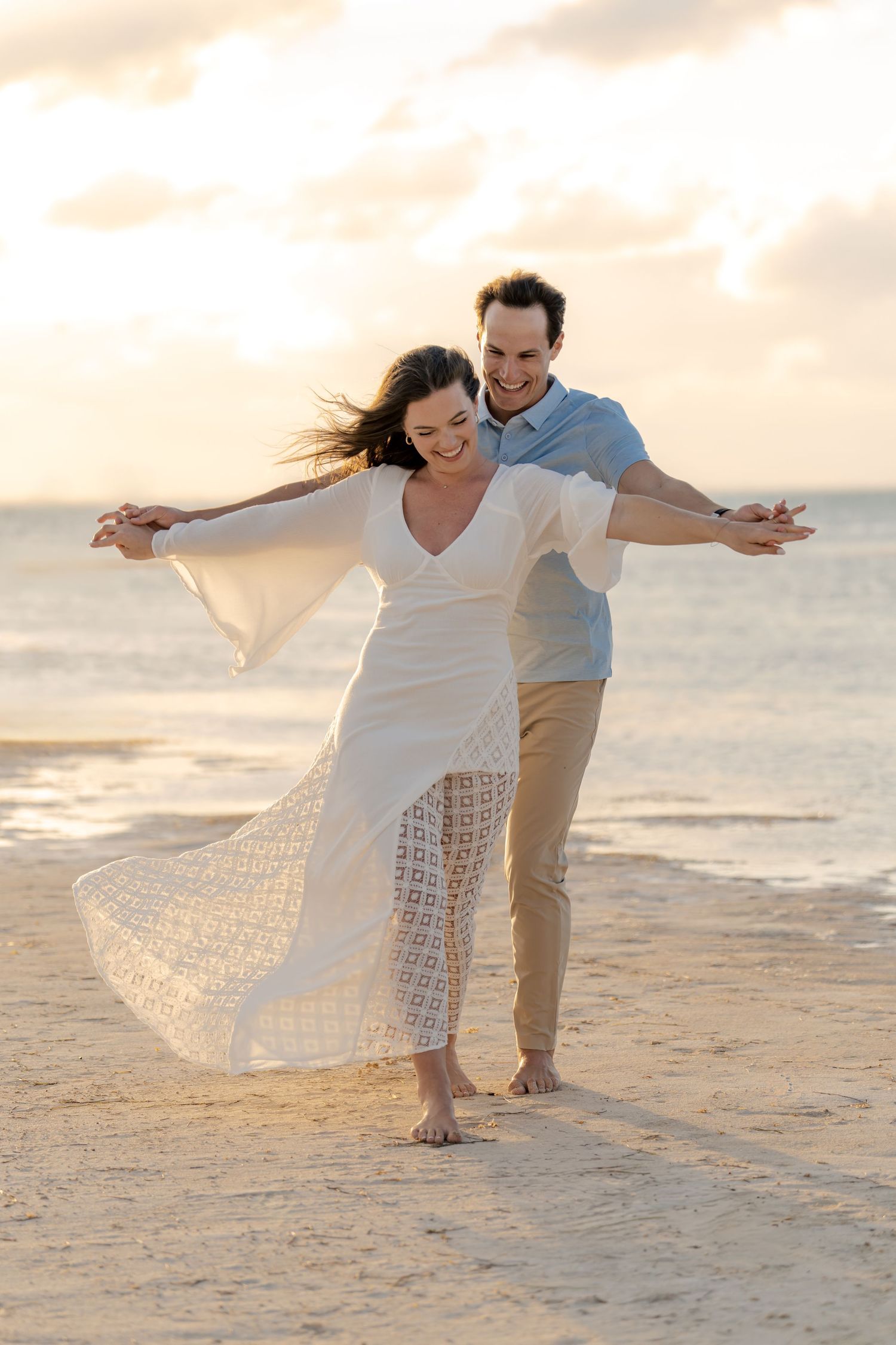 Carefree moment on beach with flowing white lace dress during sunset.