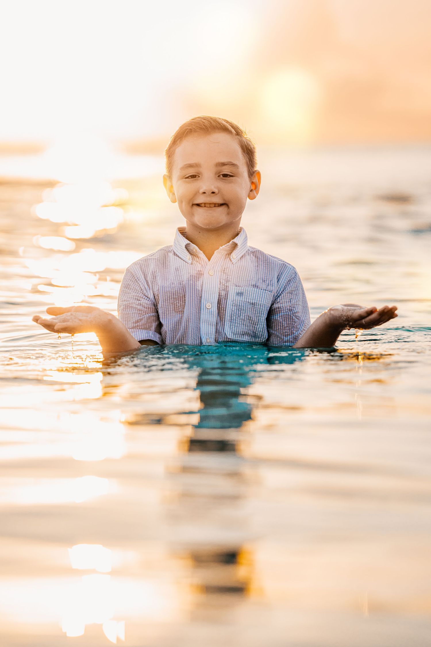 Person playing in shallow ocean water during golden sunset creating reflective ripples.