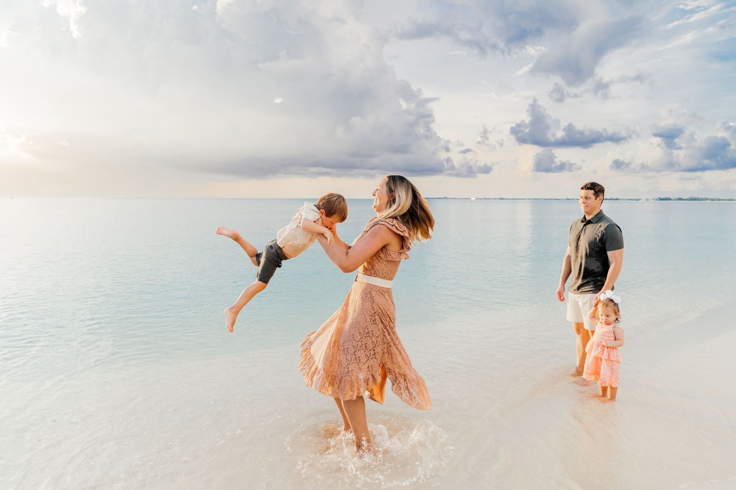 Playful family moment splashing and dancing in crystal clear tropical waters during sunset.