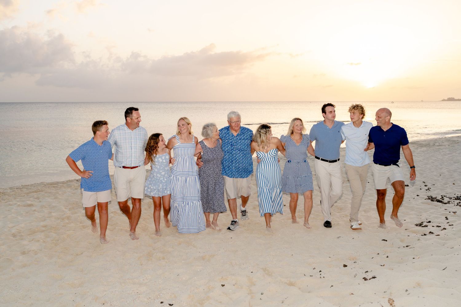 Extended family in coordinated outfits walking together on beach during sunset.