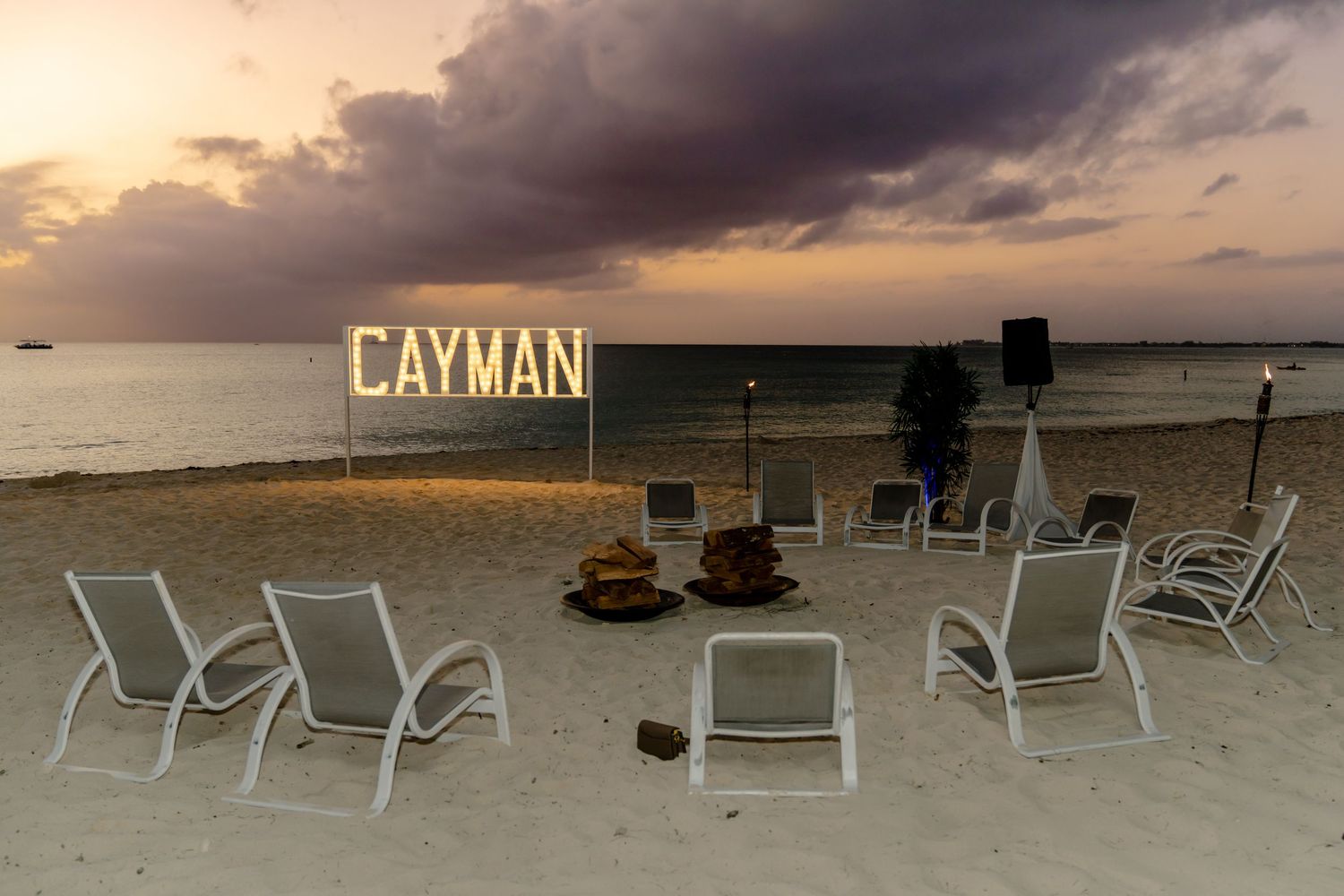 Beach lounge chairs arranged on sand with Cayman signage during golden hour.