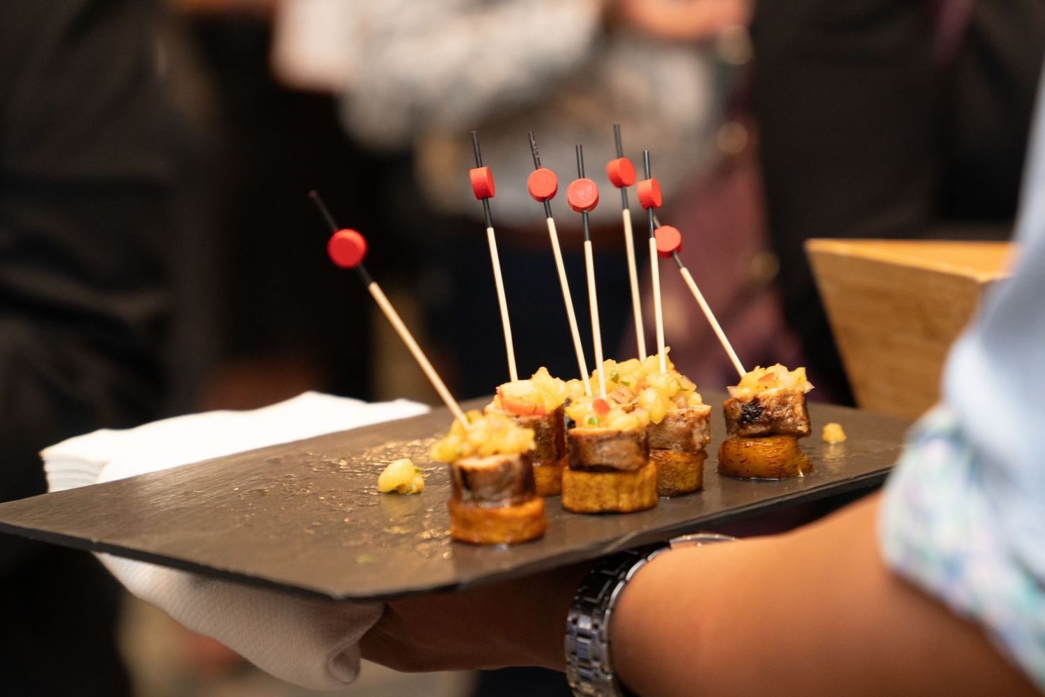 Close-up of appetizer hors d'oeuvres with toothpicks on a dark serving surface.