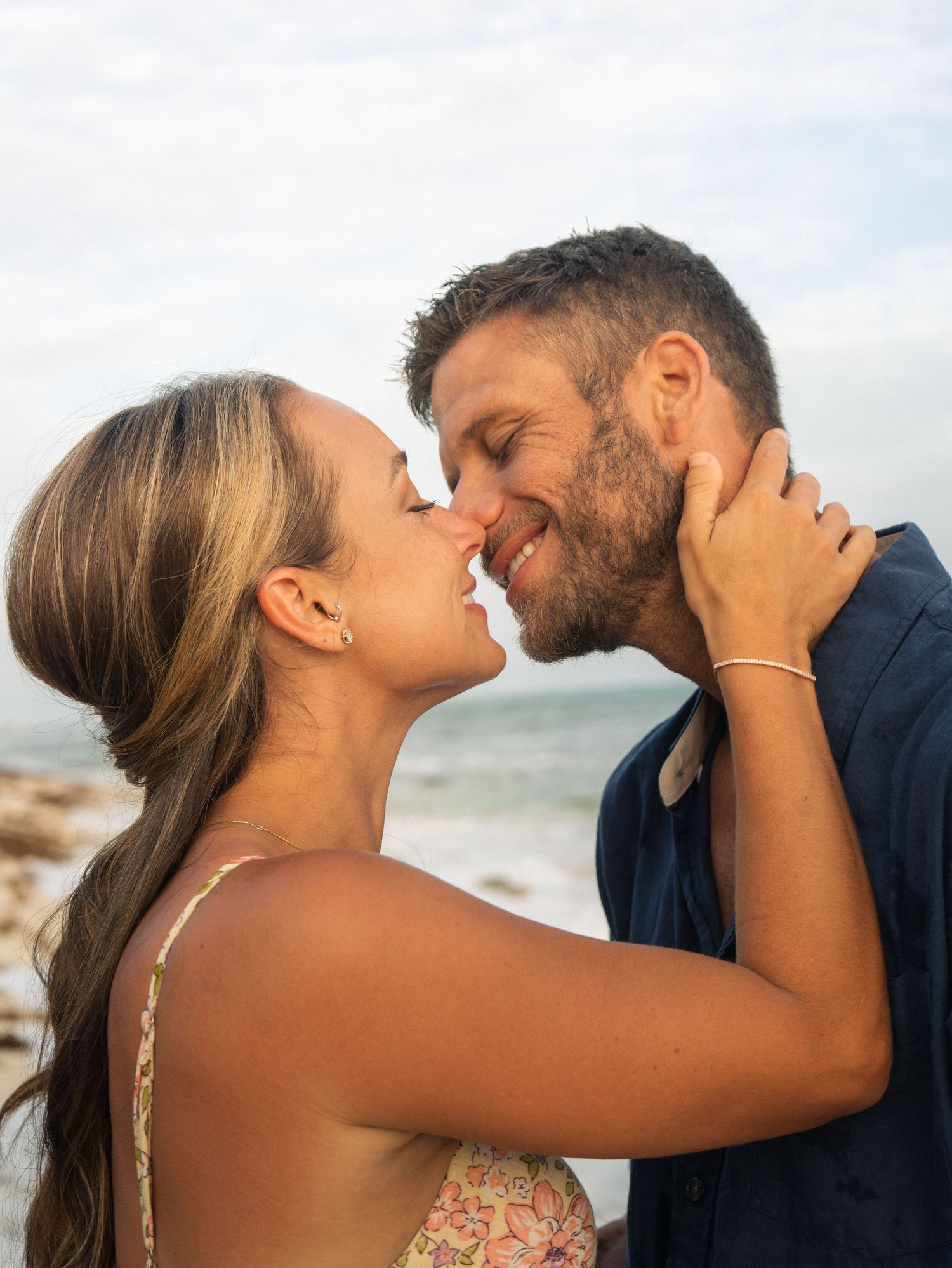 Romantic couple sharing a tender kiss on a beach with ocean waves in the background.