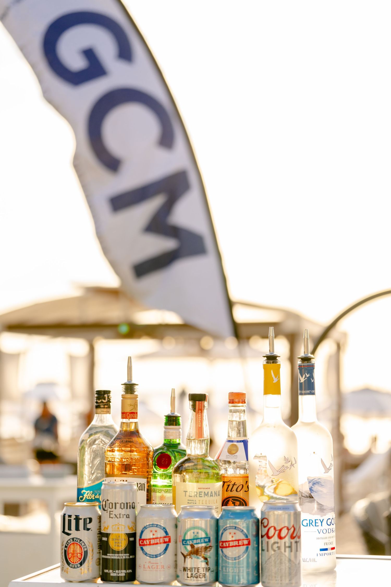 Row of liquor bottles and beer brands displayed at an outdoor beach bar setup.