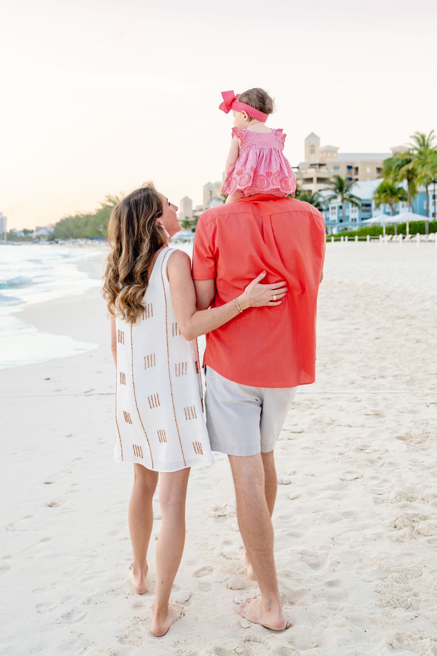 Couple walking hand in hand along a pristine beach with buildings in the background.