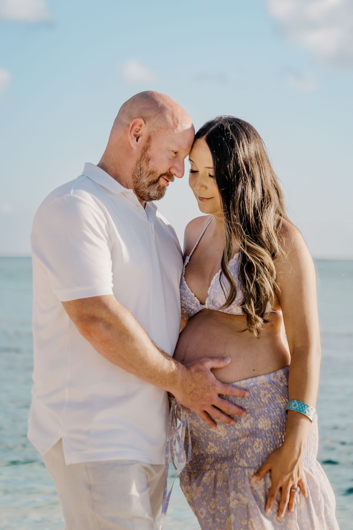 Couple sharing intimate maternity moments on beach during sunset photoshoot.
