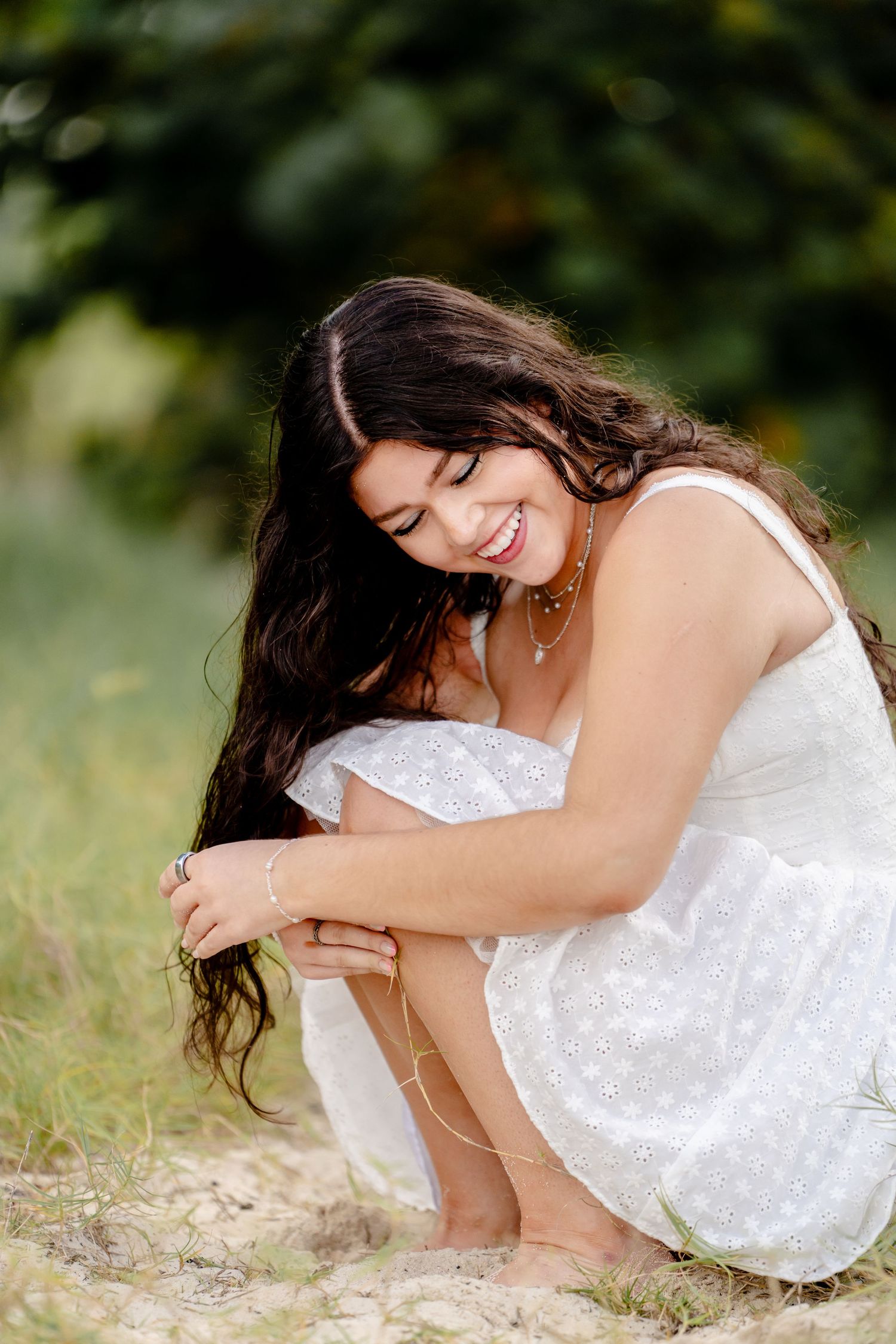 Person in white dress sitting on grass during outdoor photoshoot.