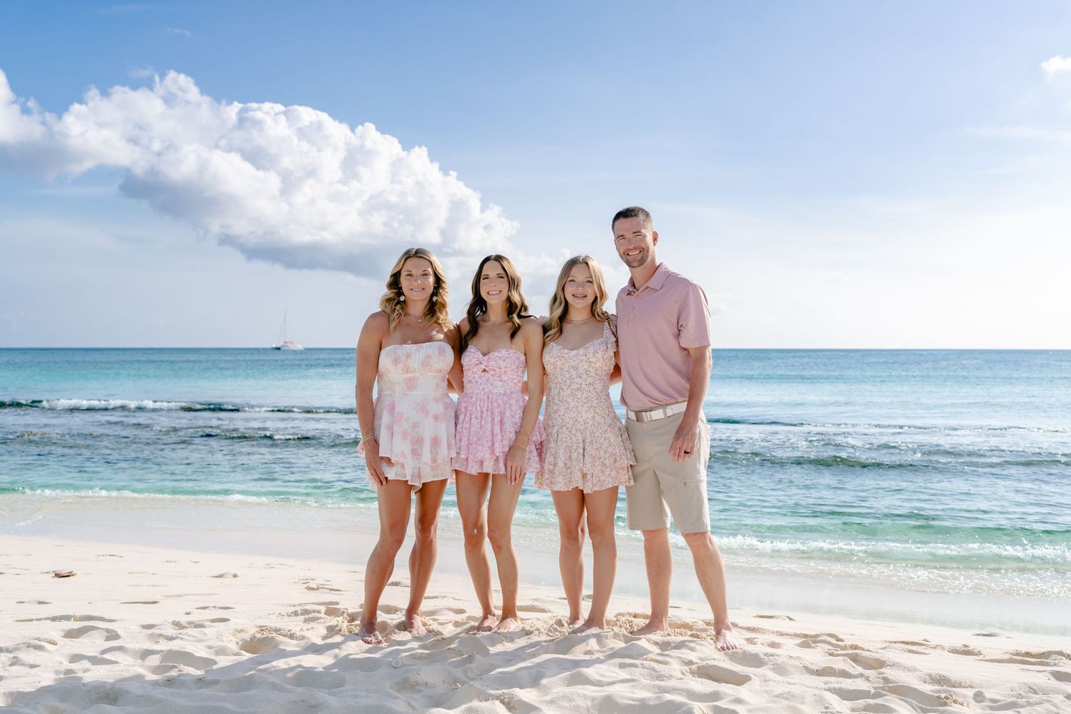 Beach family portraits with coordinated white and pink outfits against turquoise ocean backdrop.