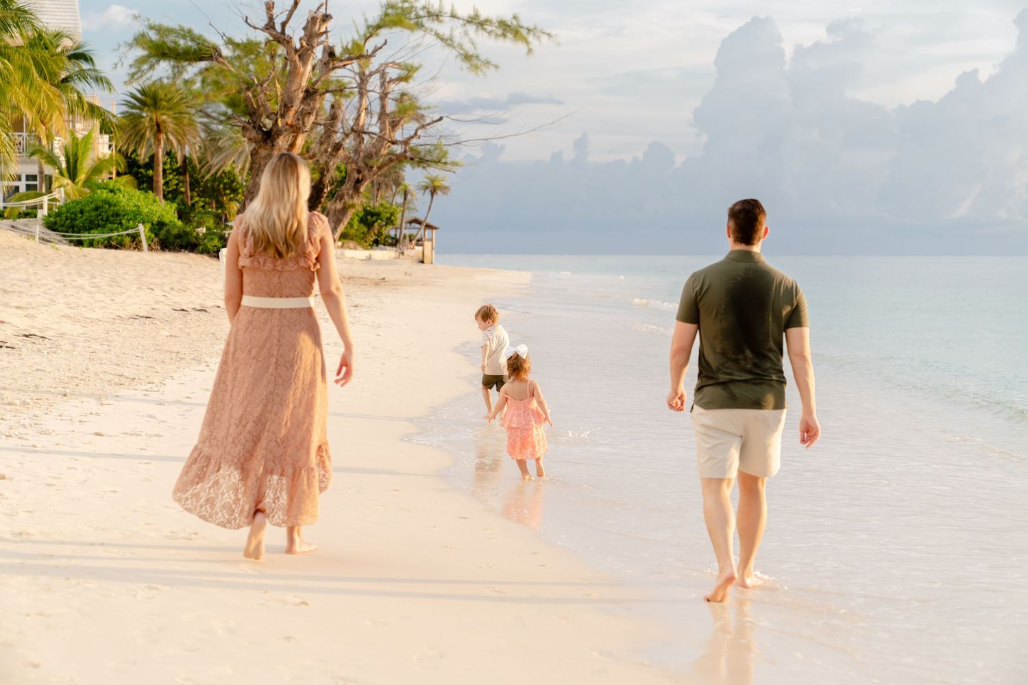 Three people taking a peaceful sunset walk along a palm-lined tropical beach.