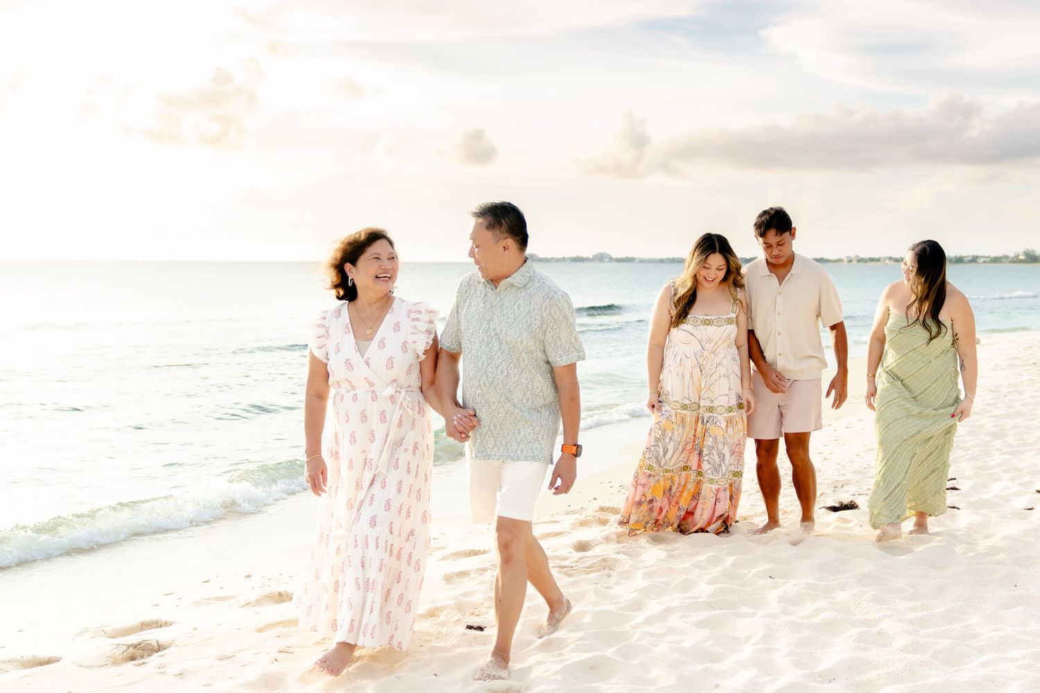 Group walking along a pristine white sand beach at sunset wearing light flowy outfits.
