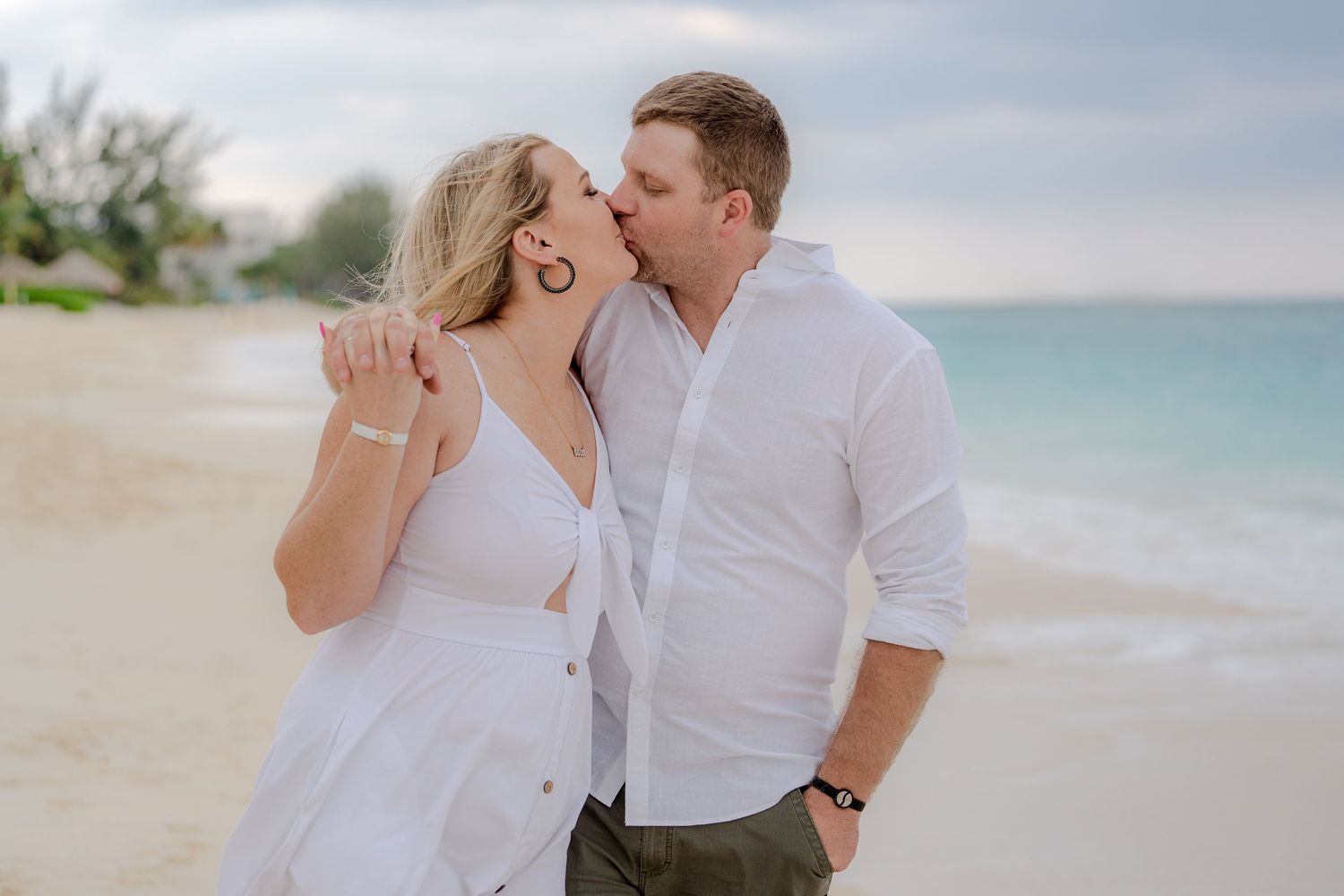 A romantic beachside moment in white outfits against turquoise waters.