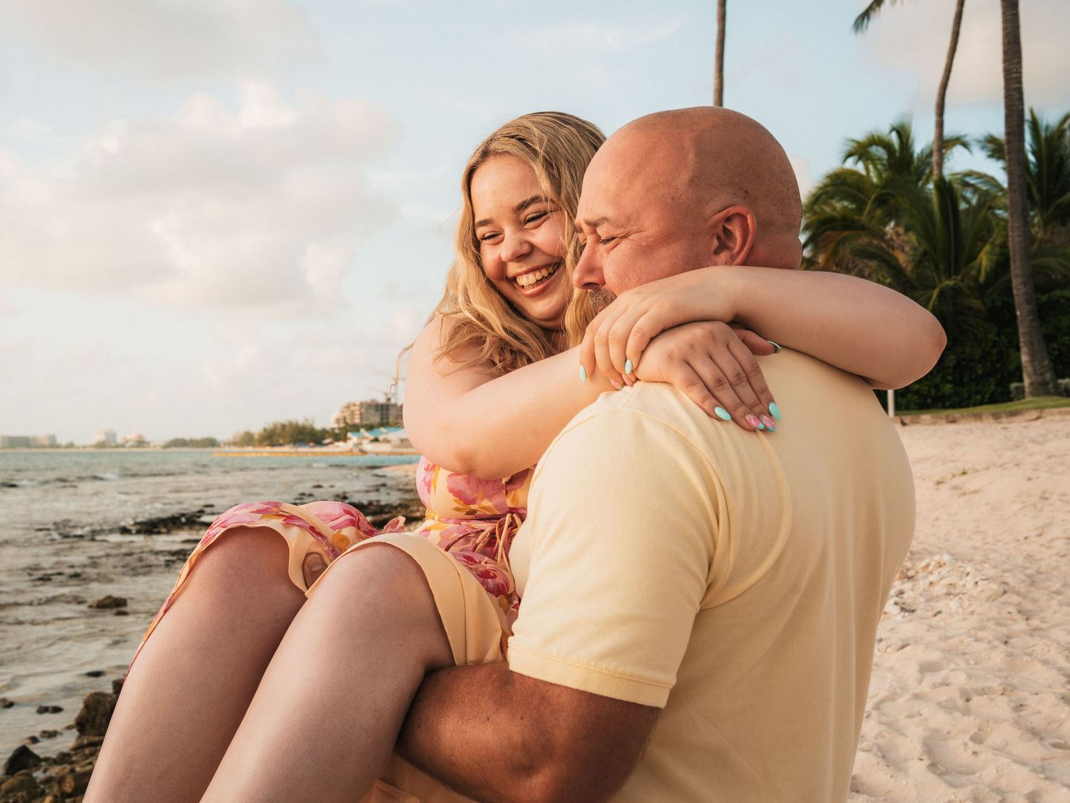 Couple embracing and laughing together on a tropical beach at sunset with palm trees in the background.