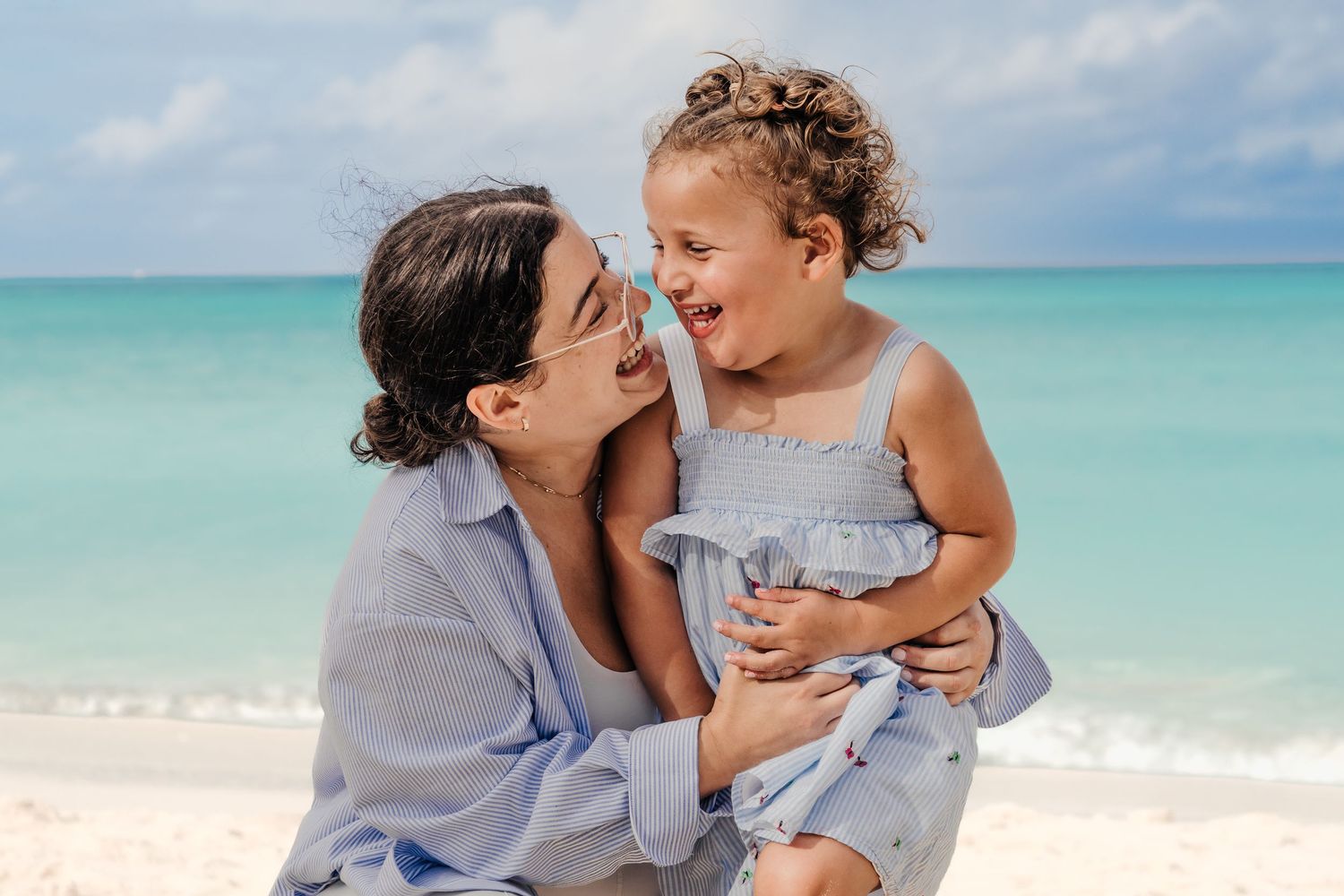 Family enjoying a tender moment together while walking along a pristine turquoise beach on a sunny day.