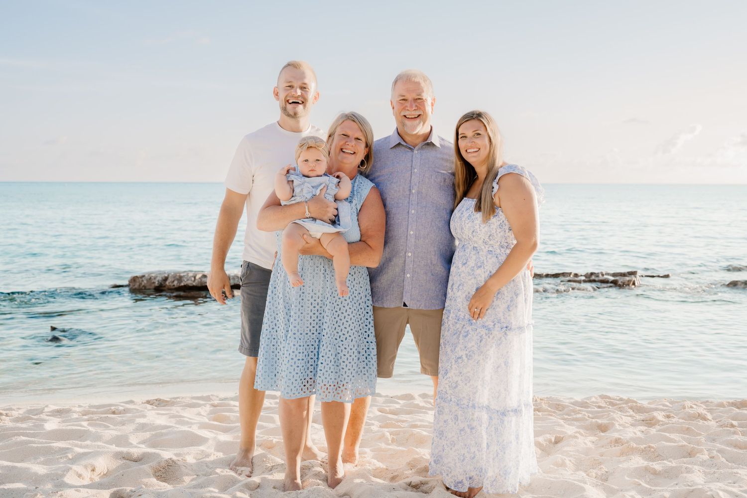 Family group wearing coordinated blue and white outfits posing on a sunny beach.