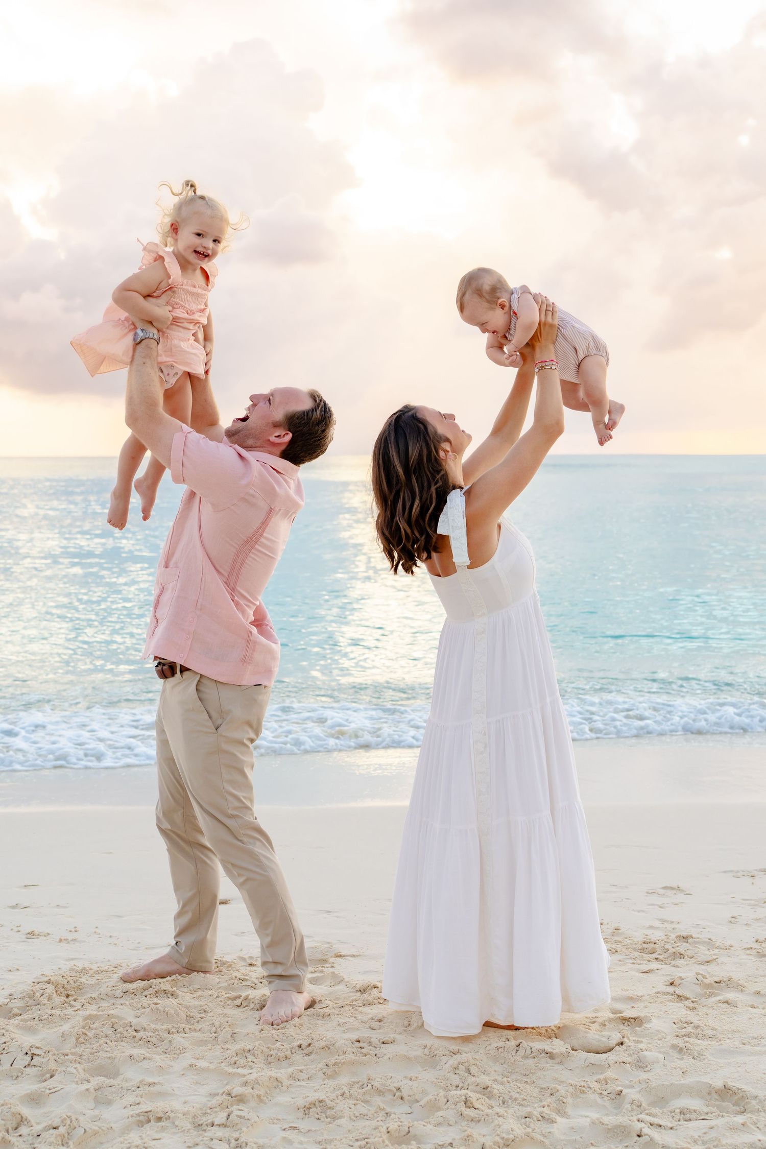 Parents lifting and playing with their baby on a sunny beach.