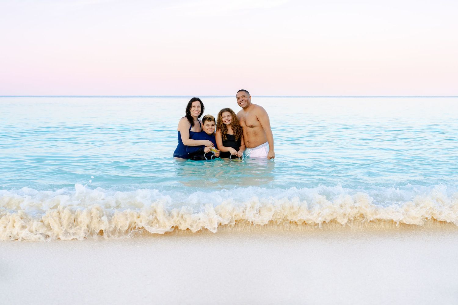 Family members playing in the ocean waves during a sunset beach session.