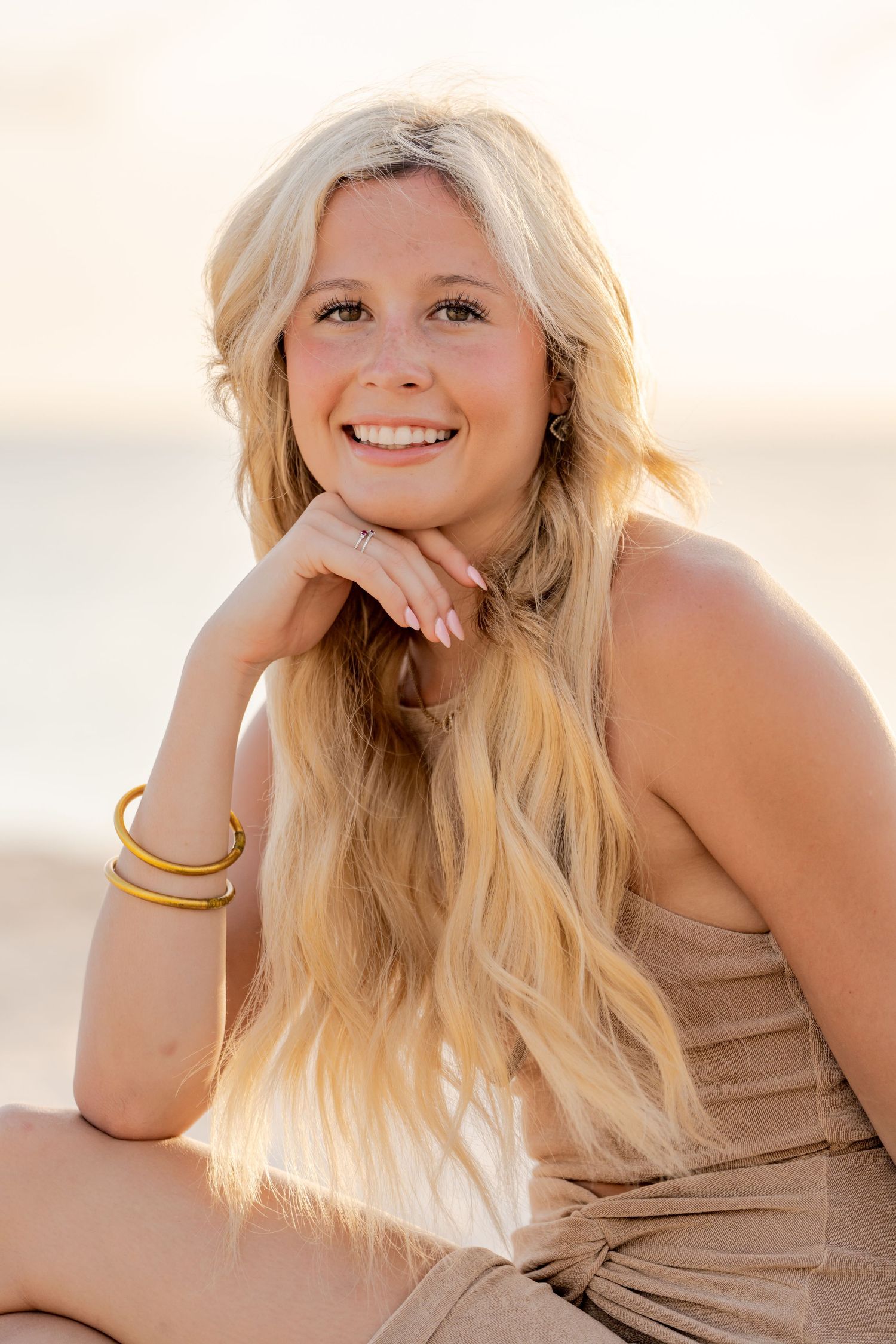 Portrait of woman with long blonde hair wearing beige dress on beach.