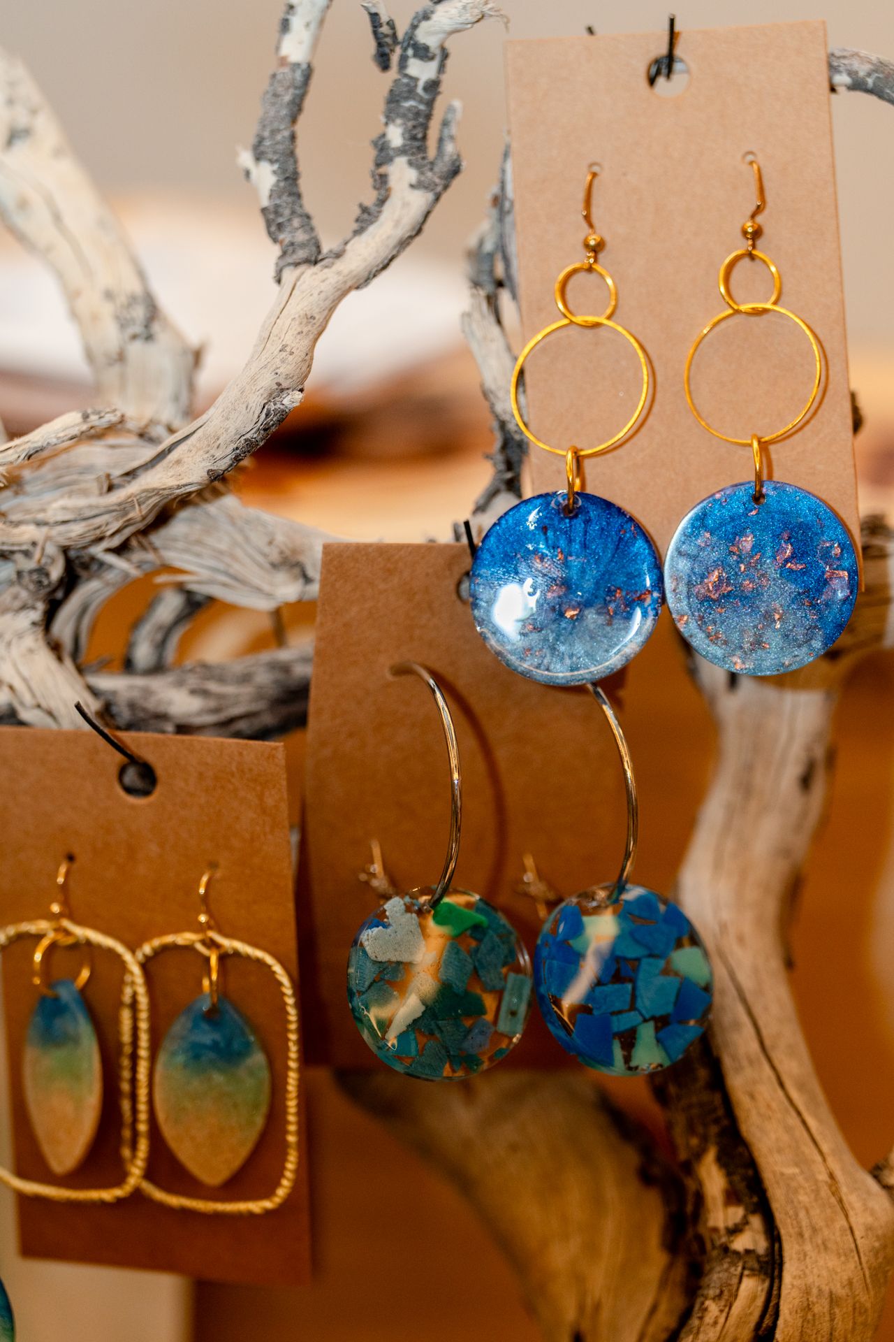 Handcrafted blue and gold earrings displayed on natural driftwood.