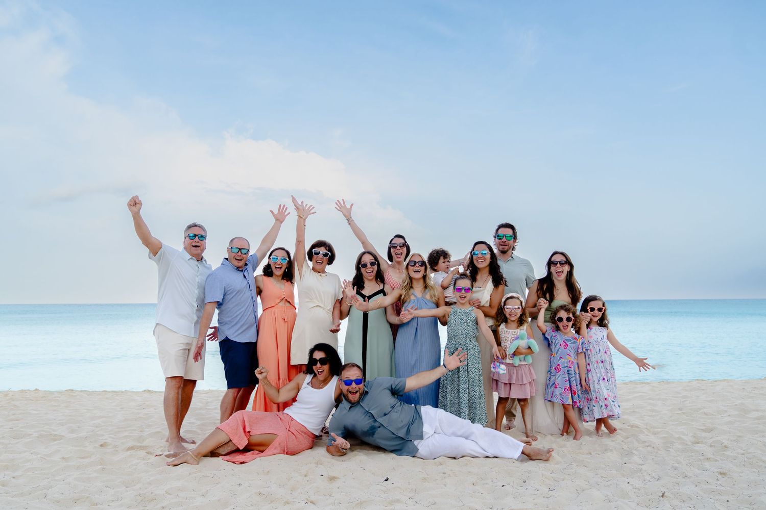 Group celebrating together on a pristine white sand beach with turquoise ocean and blue sky backdrop.