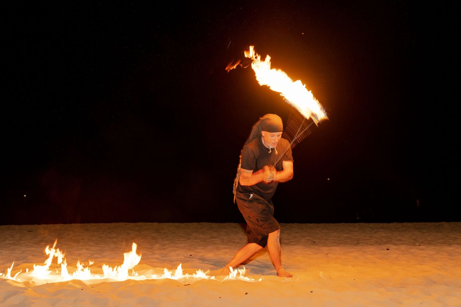 Fire performer spinning flames on a dark beach at night.