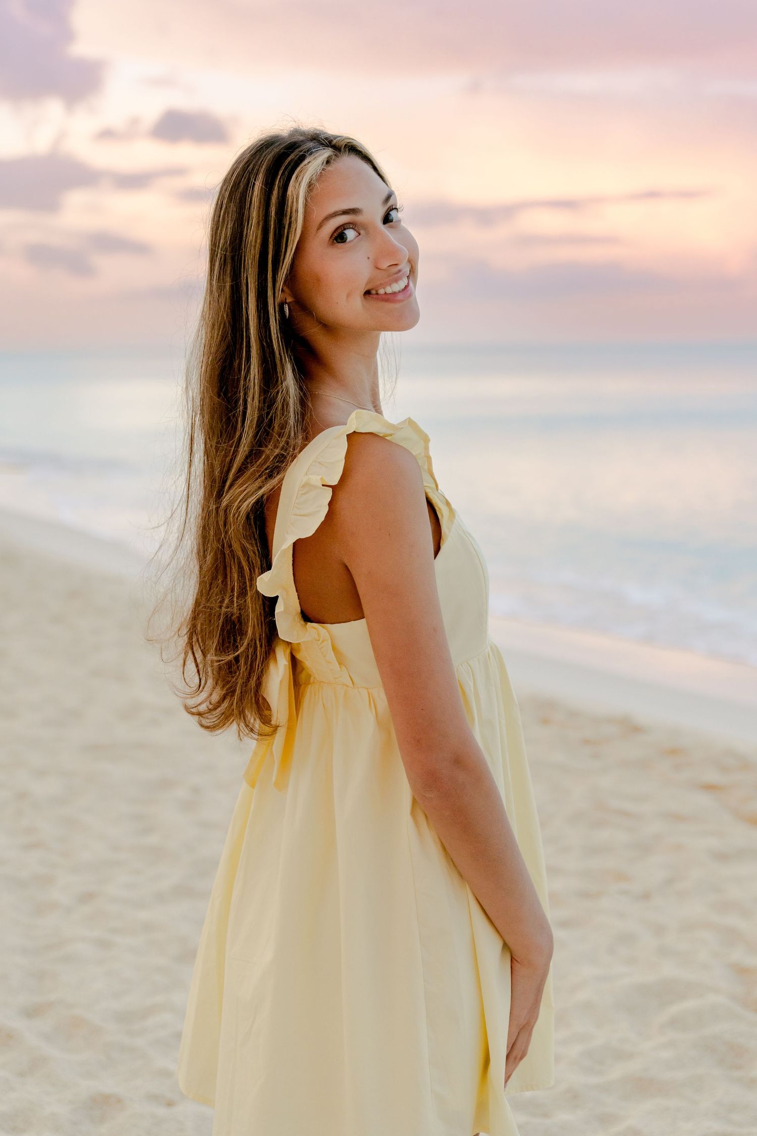 Young girl in yellow dress twirls on beach during golden hour sunset.
