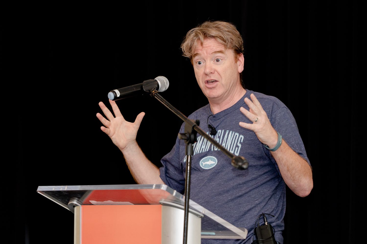 Speaker gesturing enthusiastically while presenting at conference podium.