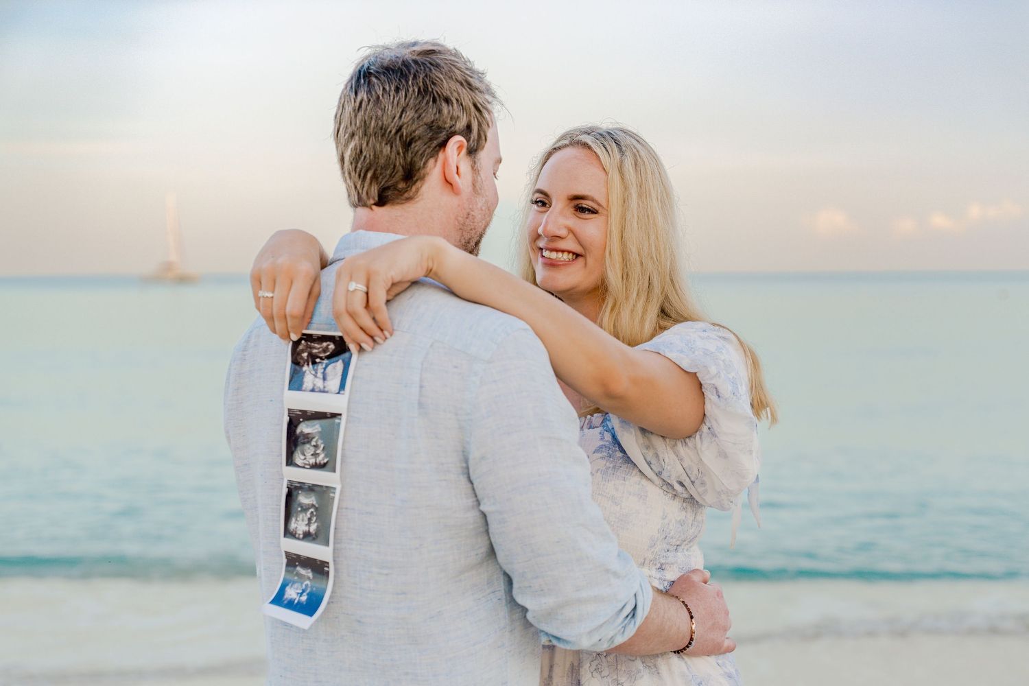 Couple holding ultrasound photos during sunset beach pregnancy announcement photoshoot.