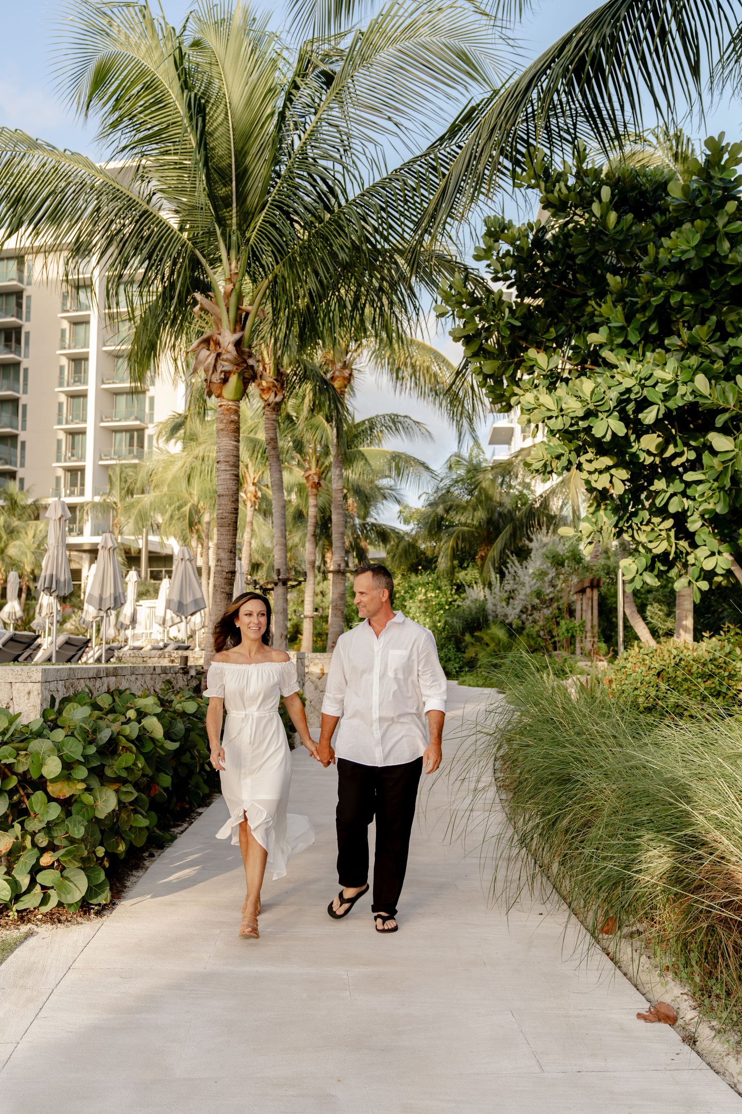 A couple strolls along a palm-lined pathway at a tropical resort.