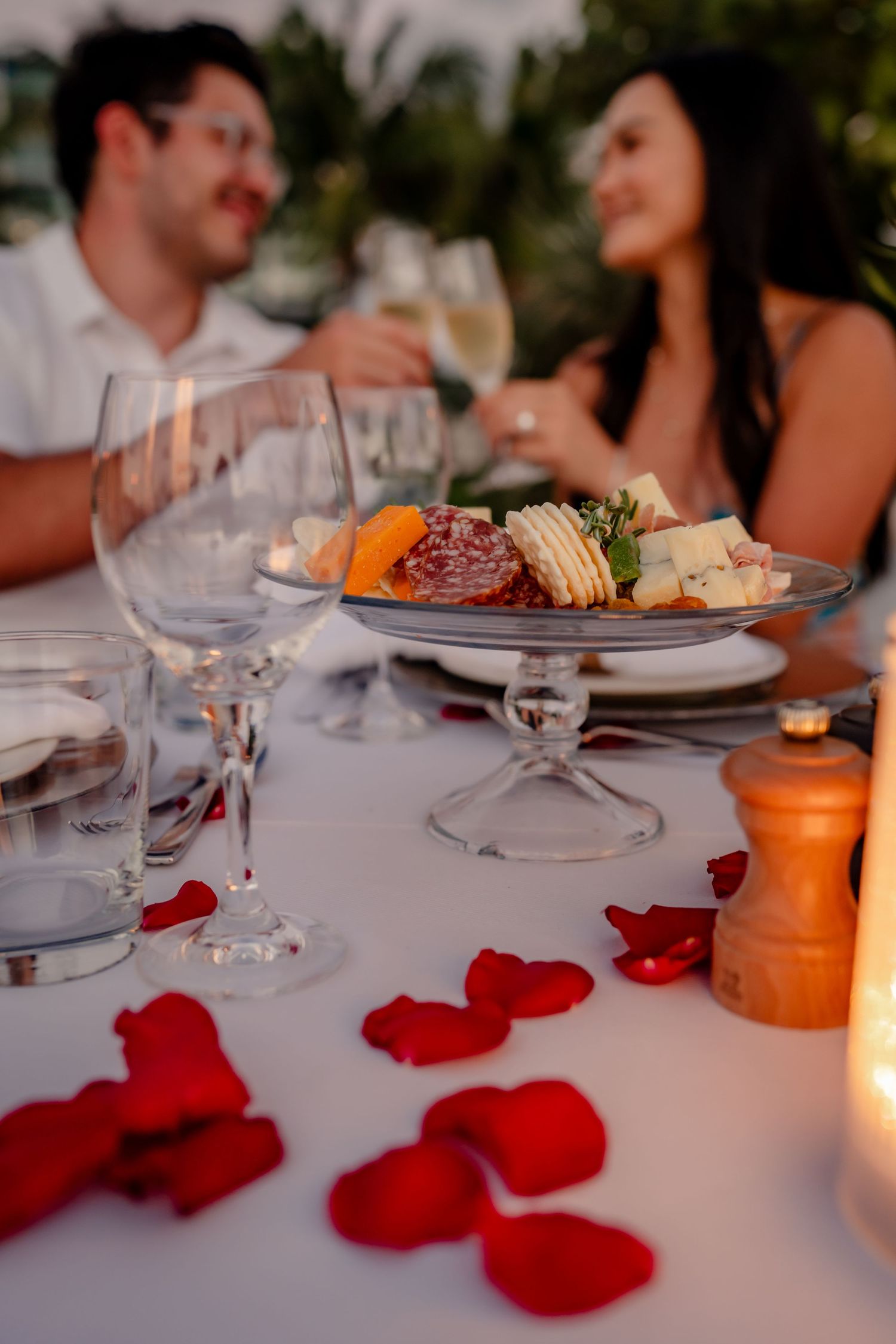 Elegant dinner table setting with red rose petals and candlelight.