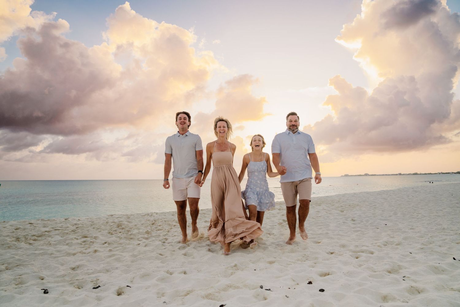 Family walking together on sandy beach during golden hour with dramatic cloudy sky.