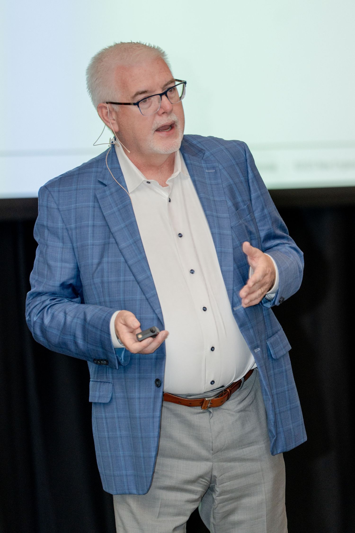 Presenter in a plaid blazer gesturing expressively during a business conference talk.