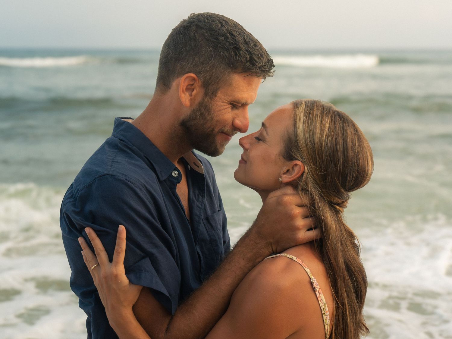 Romantic couple embracing on a beach with ocean waves, sharing an intimate moment near the water.