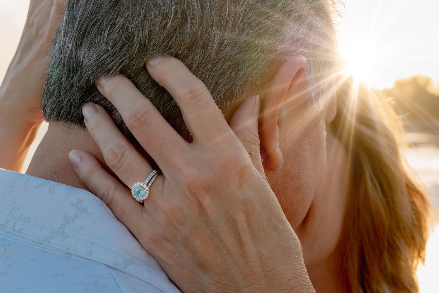 Woman showing diamond engagement ring while embracing partner in golden sunset light.