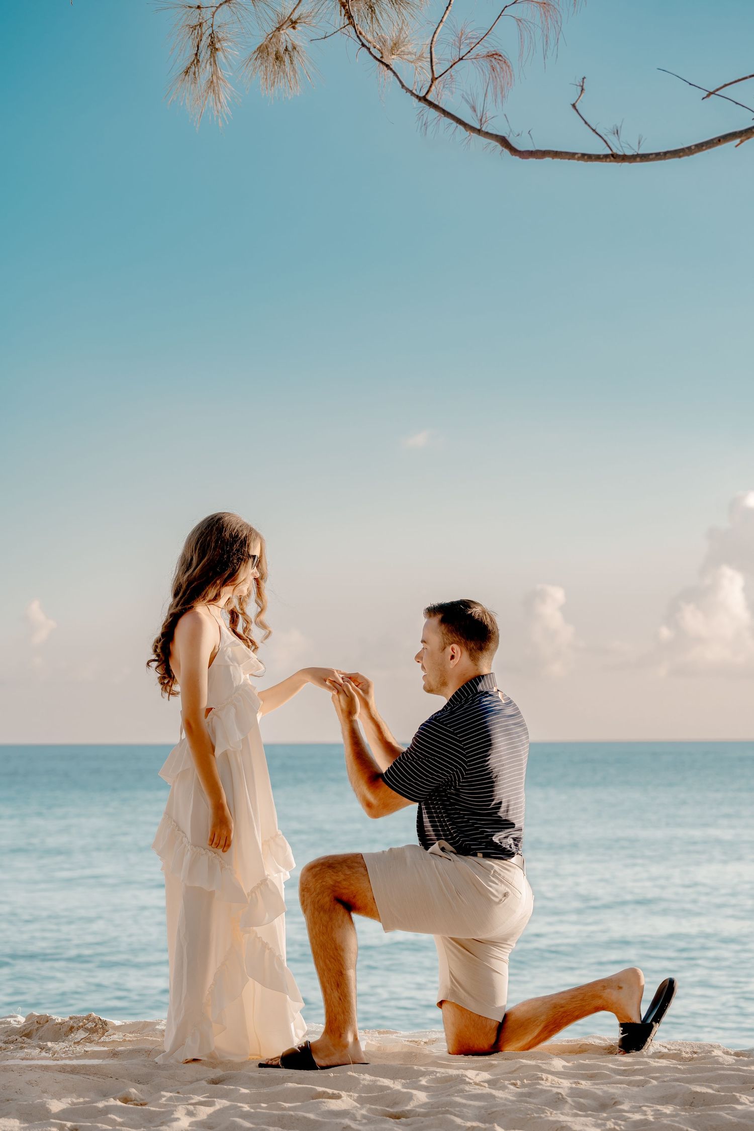 Beach proposal scene with ocean backdrop and clear blue skies.