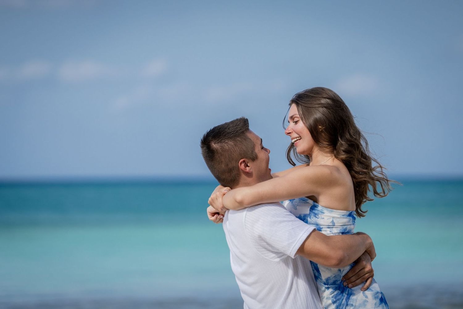 Intimate beach portraits with turquoise ocean waves and soft clouds in background.