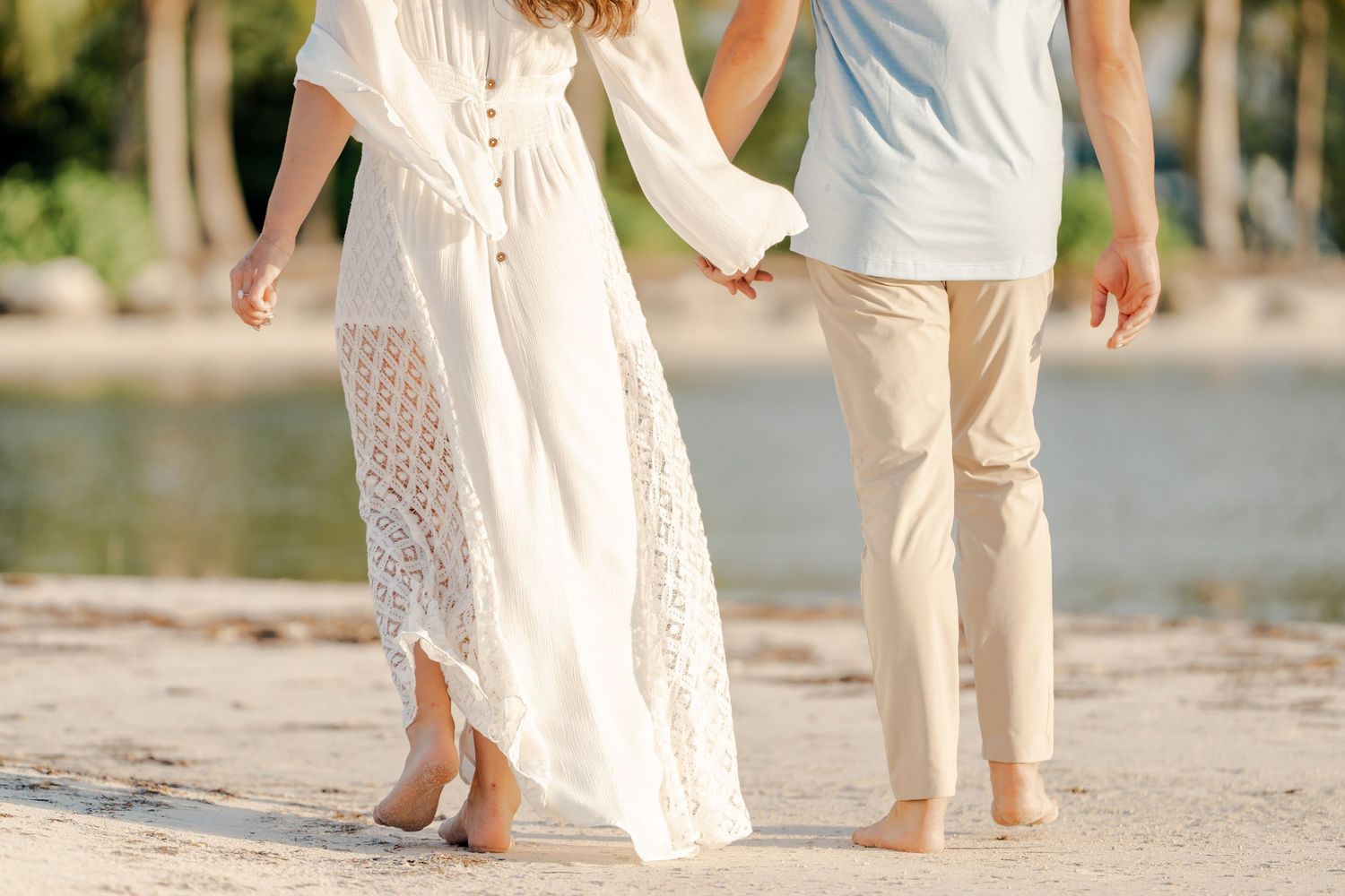 Close-up of couple's feet walking together on beach with white dress and khaki pants.