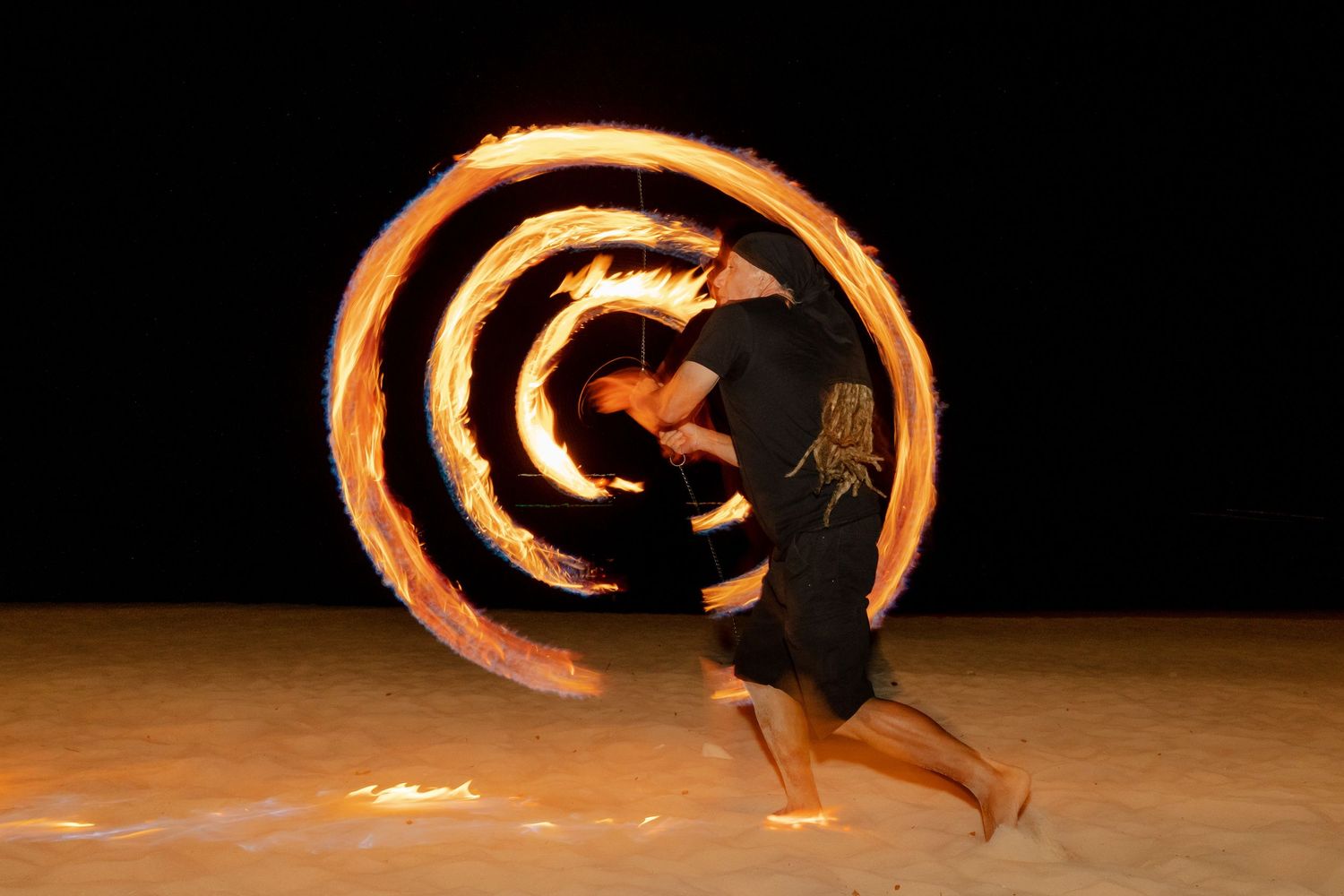 Fire dancers perform mesmerizing moves with flaming props against a dark background.