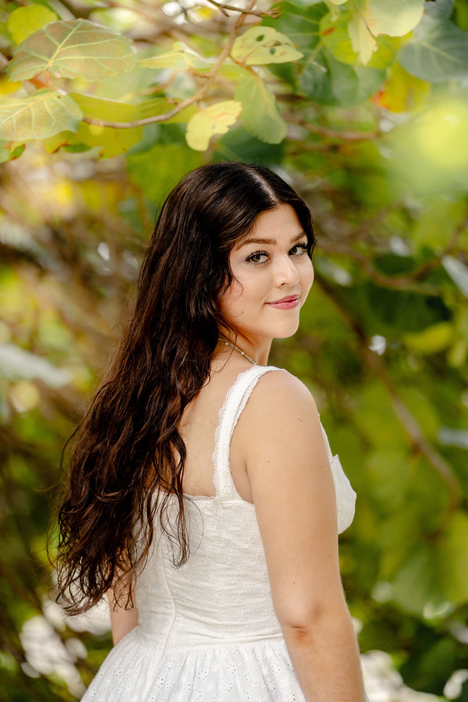 Candid outdoor photography session among green leaves wearing white summer dress.