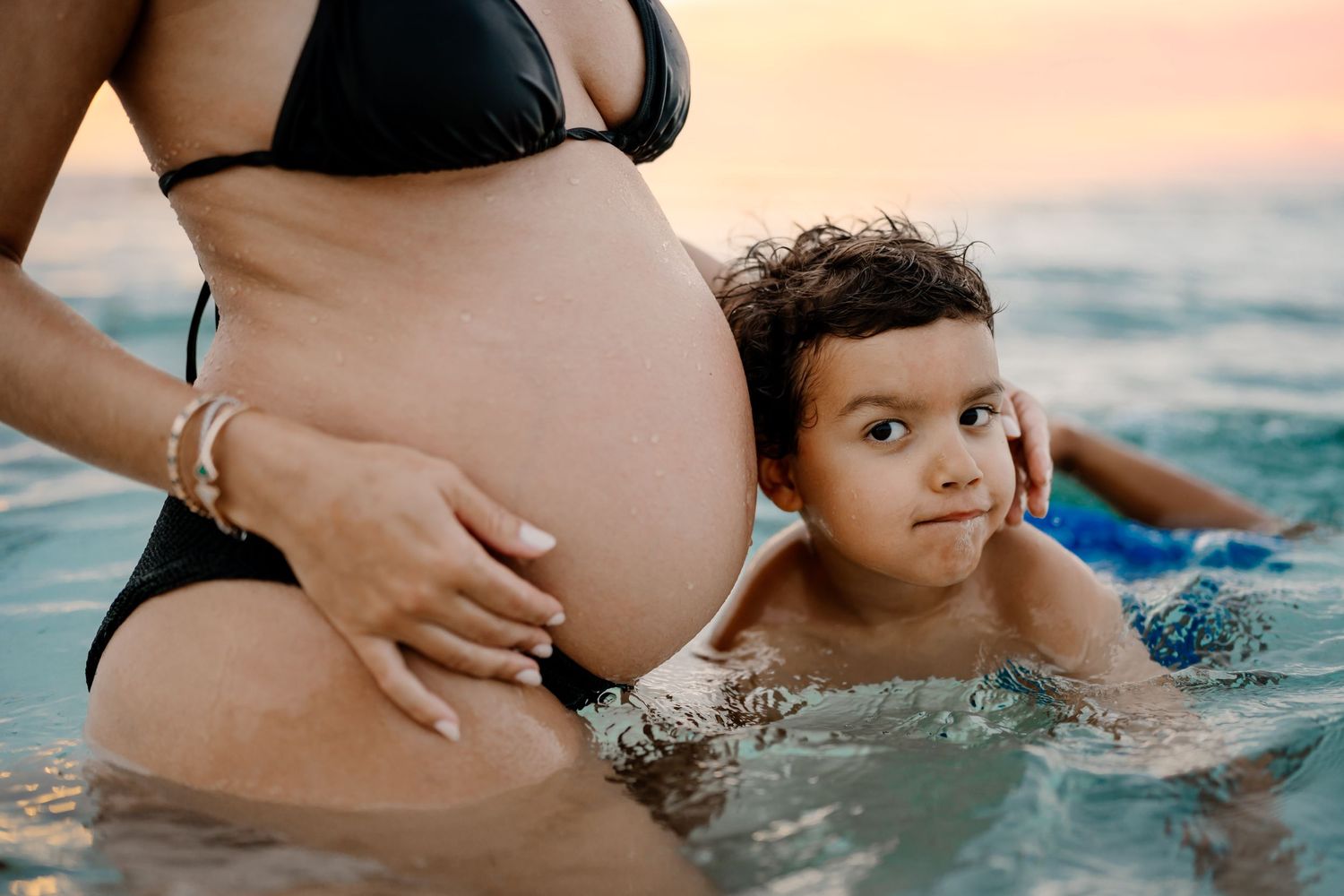 Maternity beach photoshoot during sunset with waves crashing on the shore.