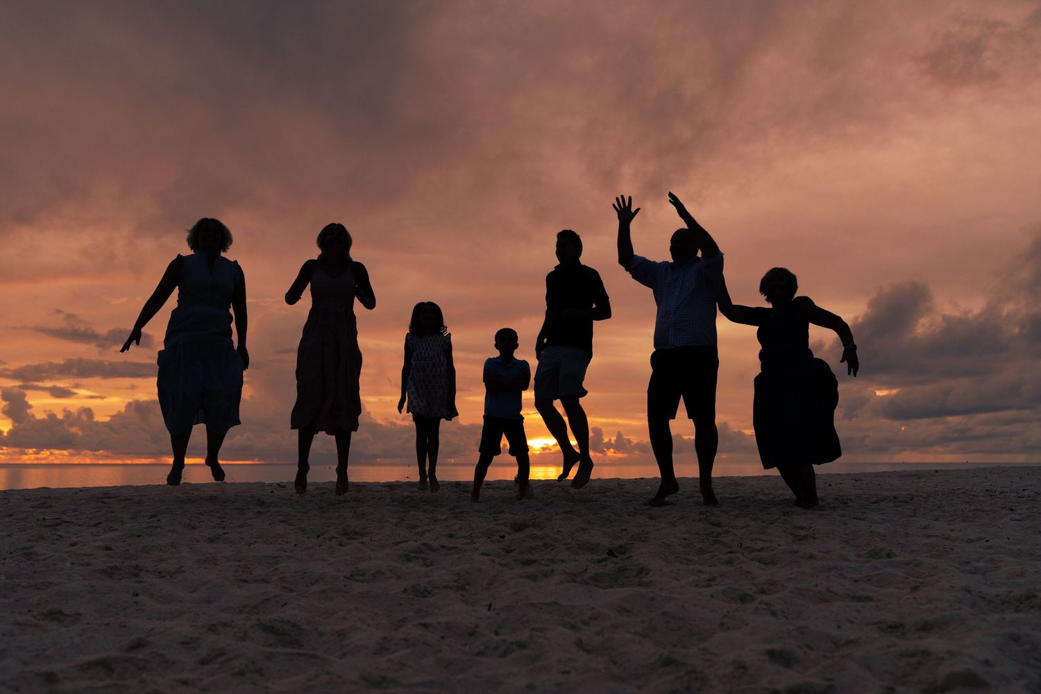 Silhouettes of people standing on a hill against a dramatic sunset sky with orange and purple clouds.