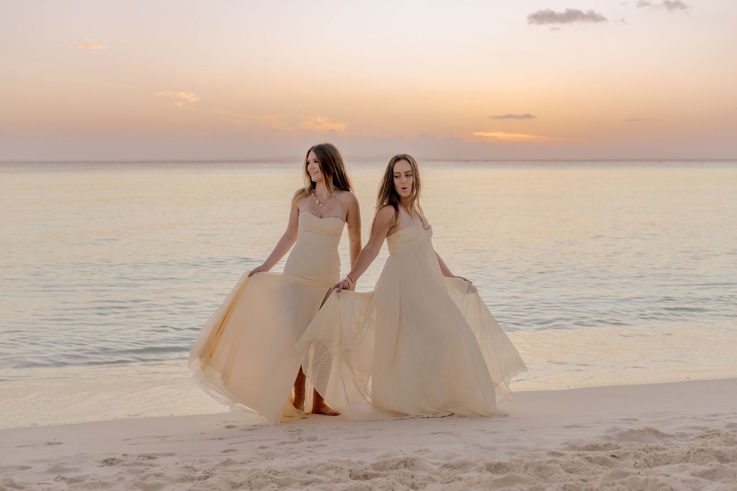 People in flowing dresses dance and twirl on a beach during sunset.
