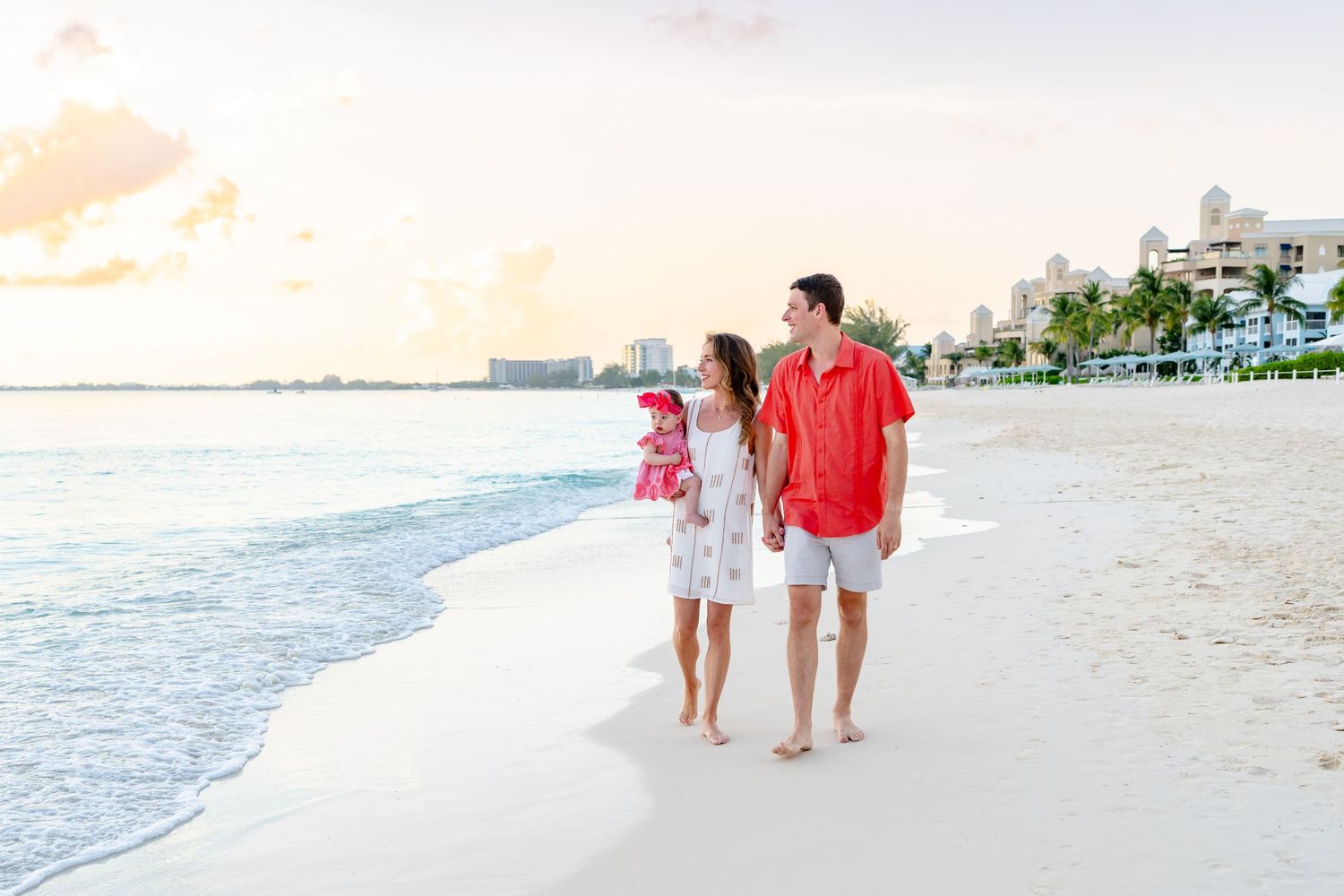 Family walking along a scenic beach with calm waters and palm trees.