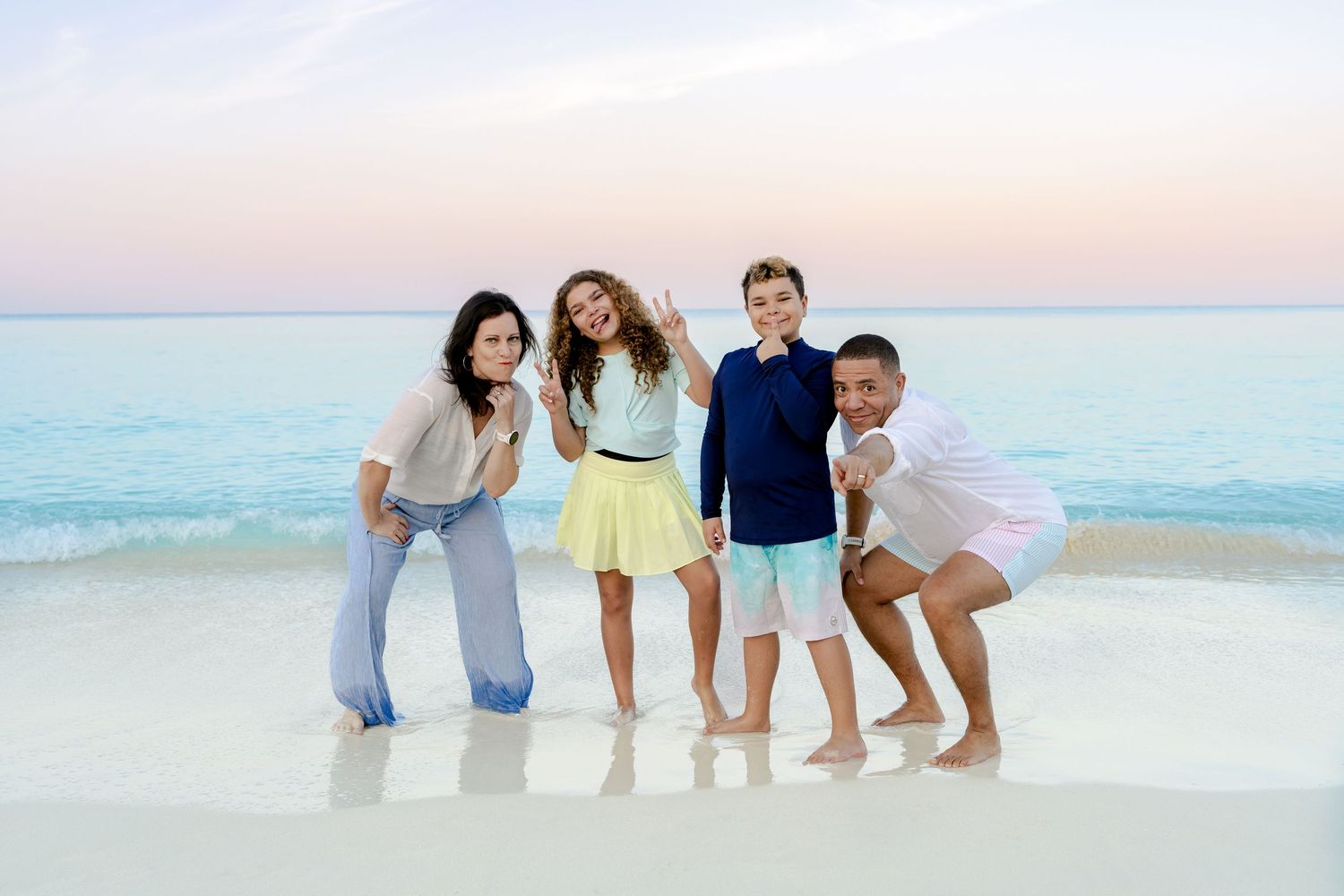 Extended family posing together on a scenic beach during sunset with soft pastel sky.
