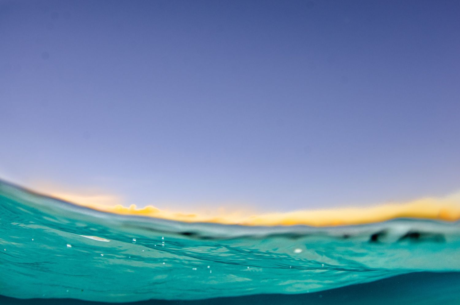 Split view of ocean horizon showing calm waters meeting bright blue sky.