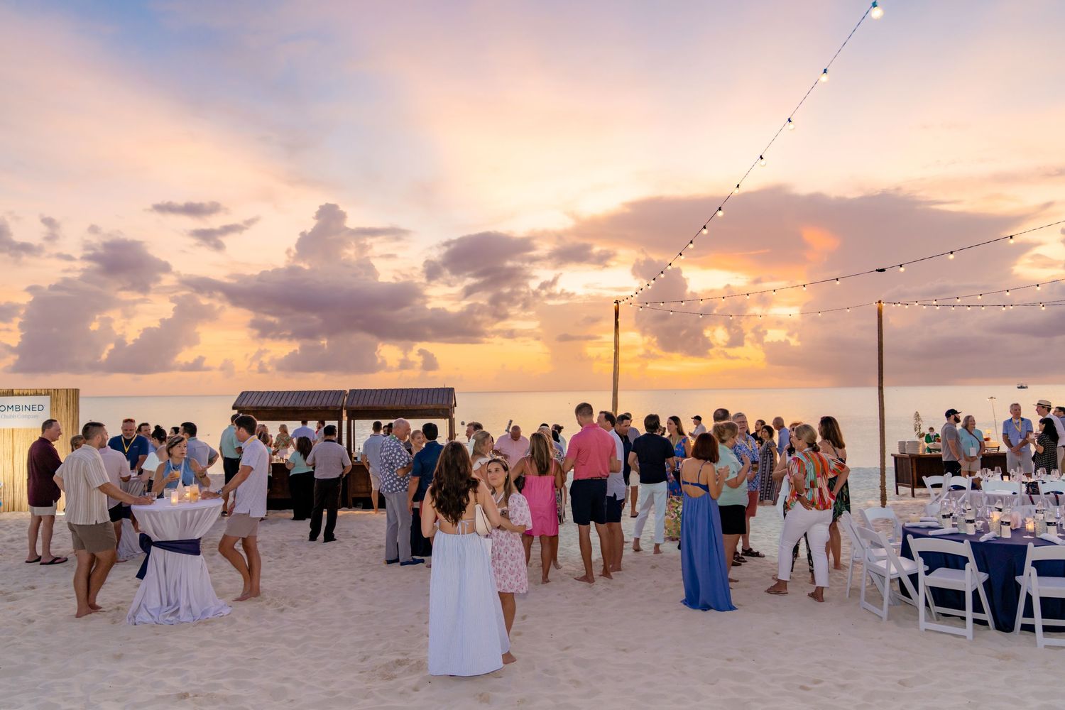 Beach wedding ceremony setup with guests gathered at sunset.