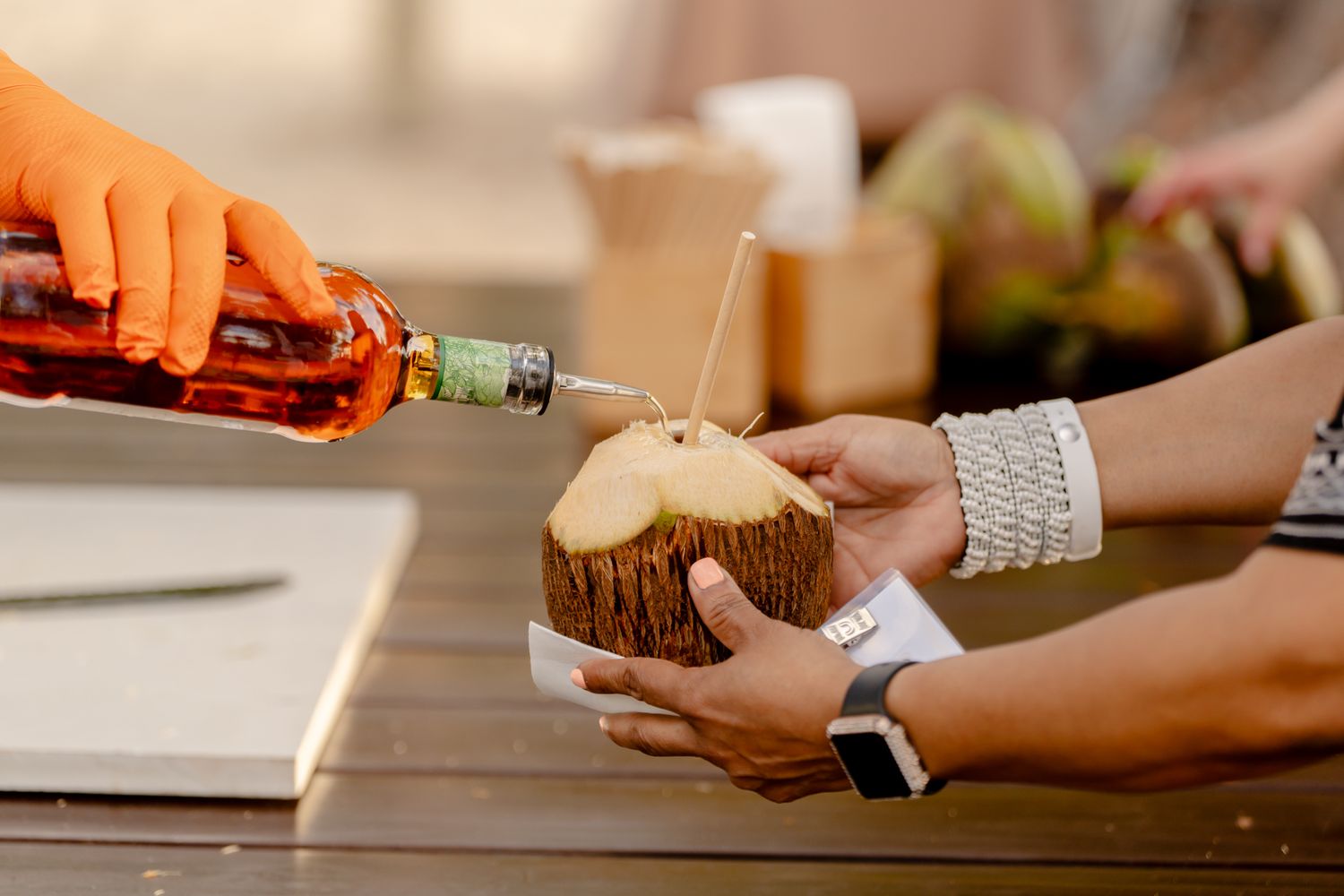 Hands holding and serving tropical coconut drinks at a beach bar.