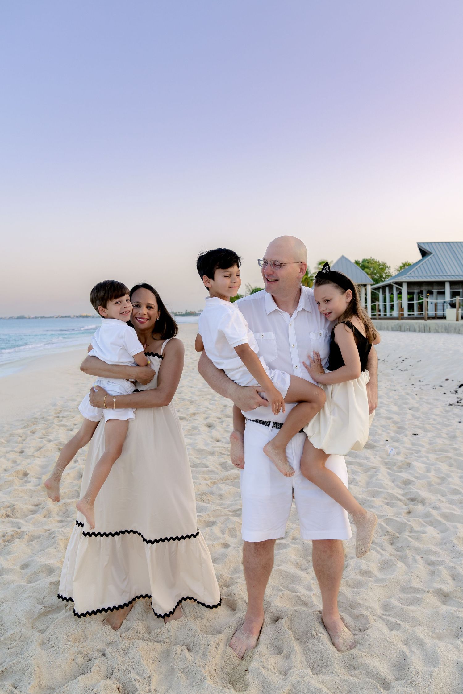 Family enjoying playful moments together on a white sandy beach at sunset.