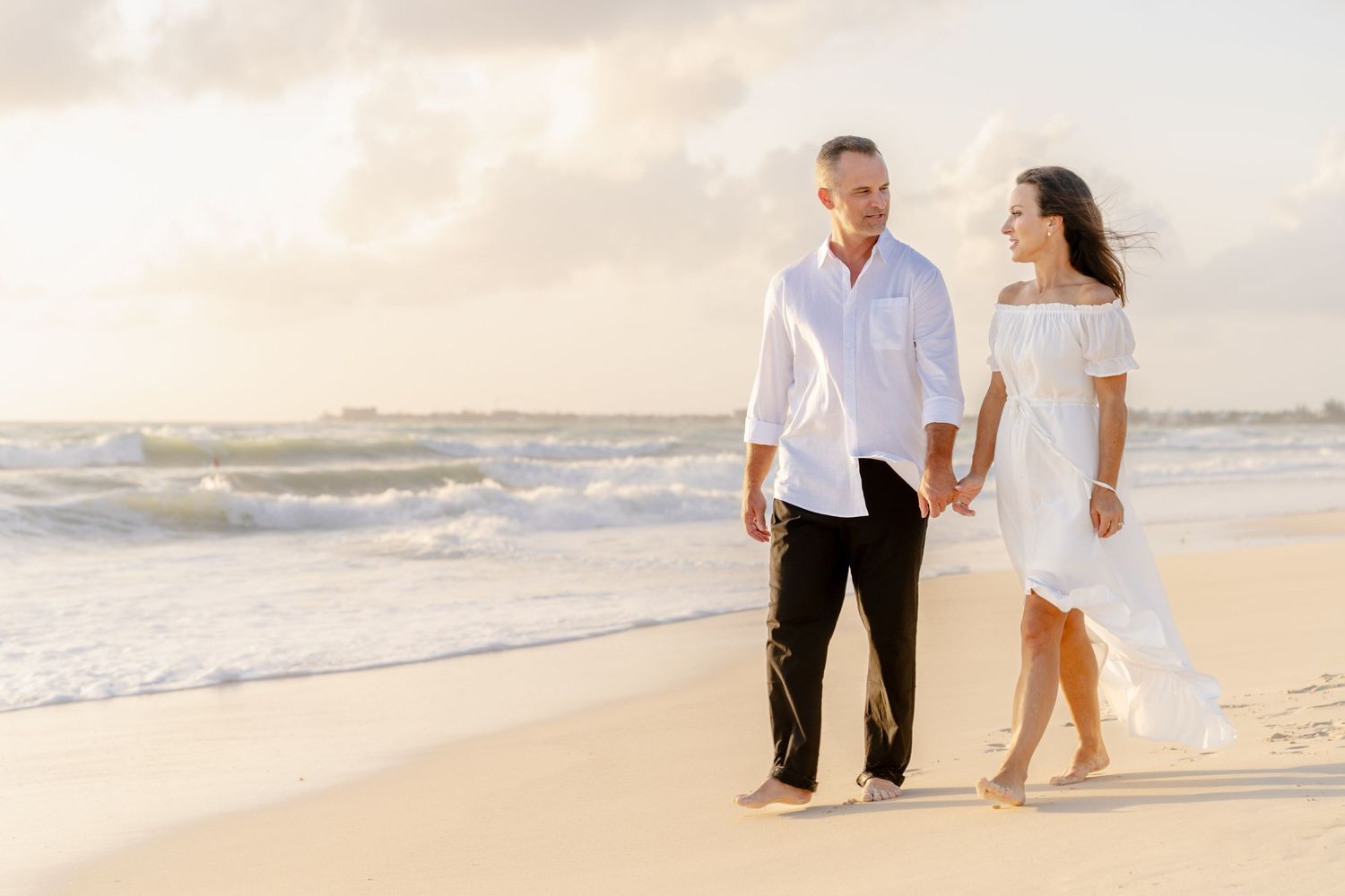 A couple walks hand in hand along a pristine beach during golden hour.