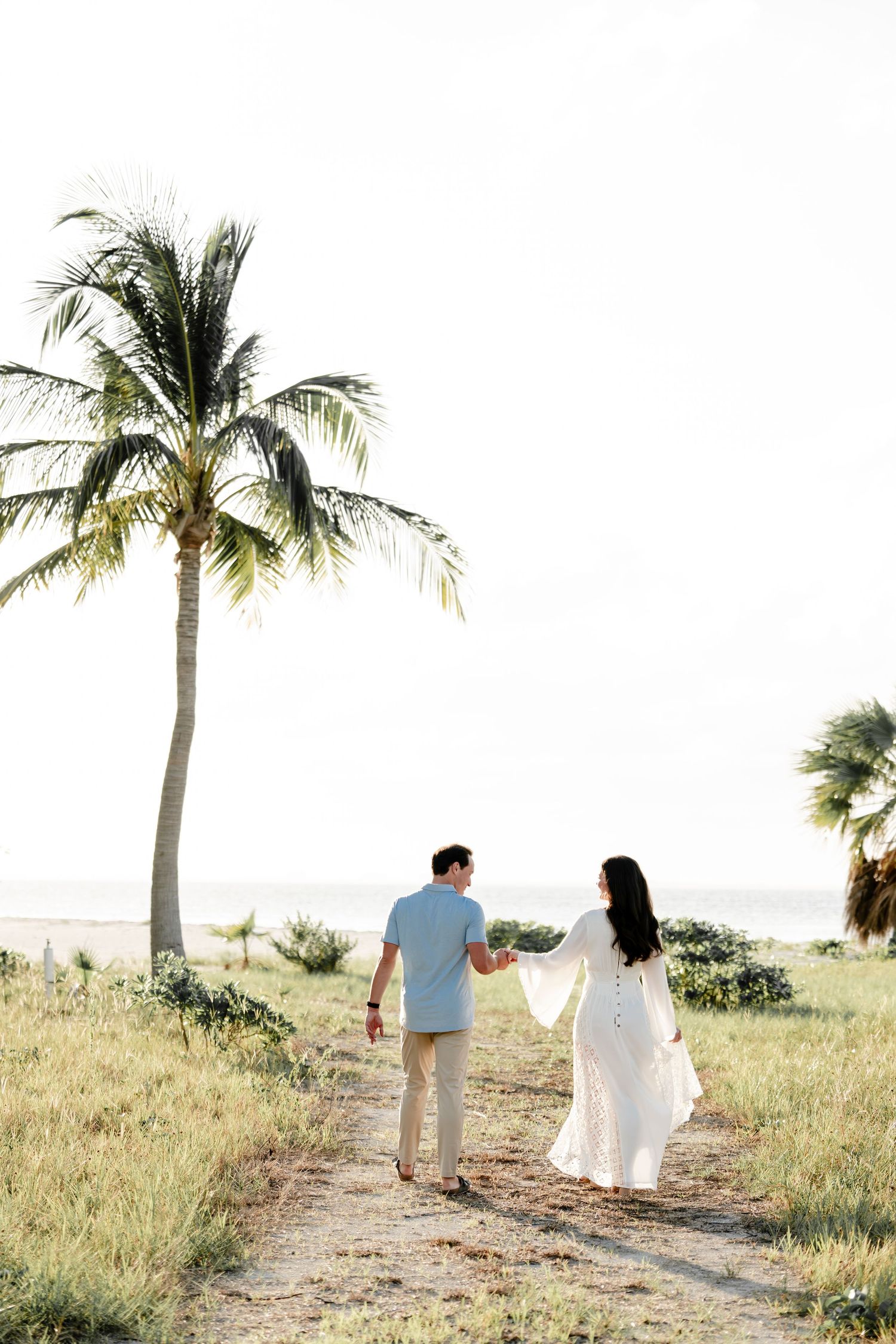 Couple walks hand in hand on path beneath palm trees in tropical setting.