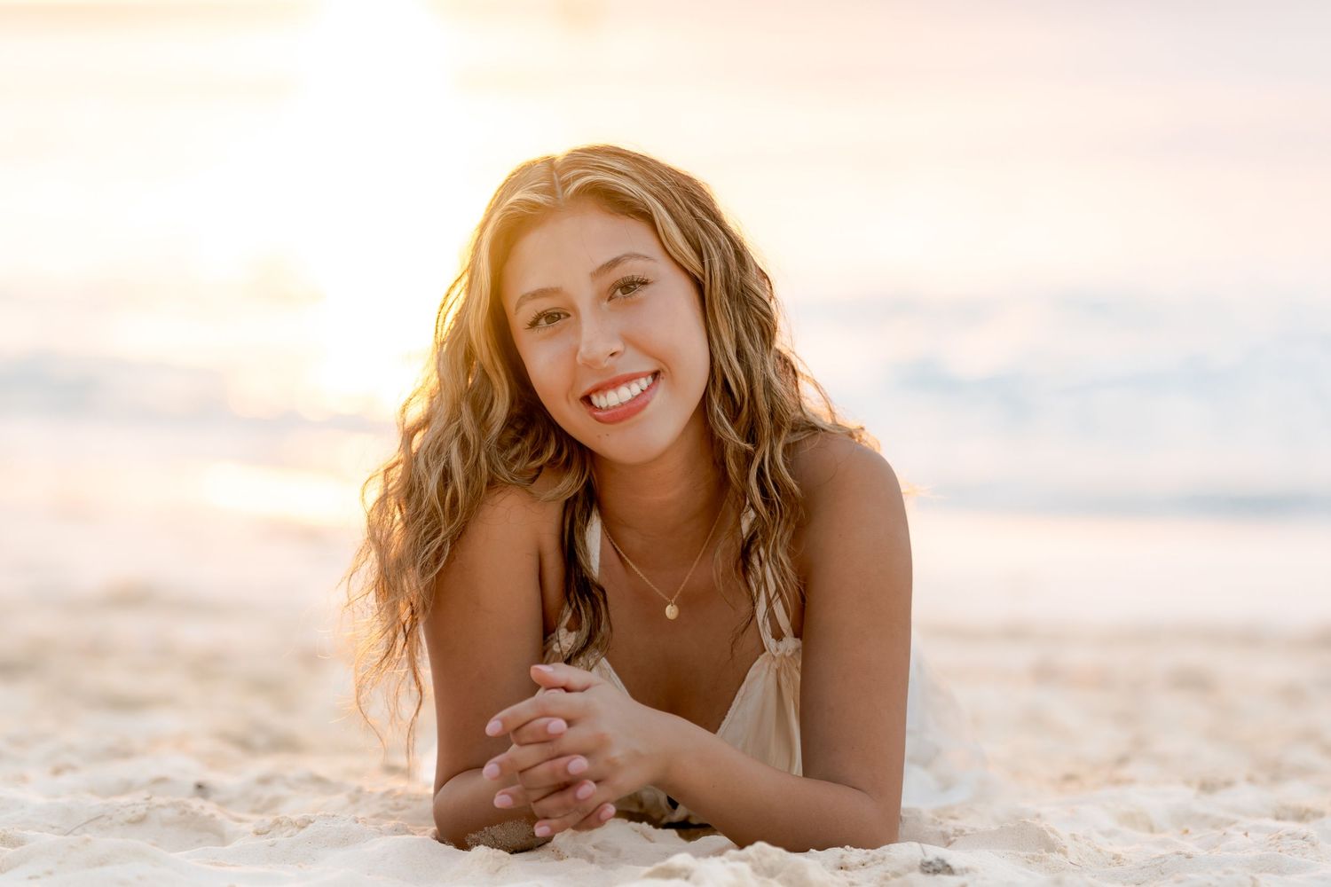 Woman in casual attire poses on sandy beach during golden sunset hour.